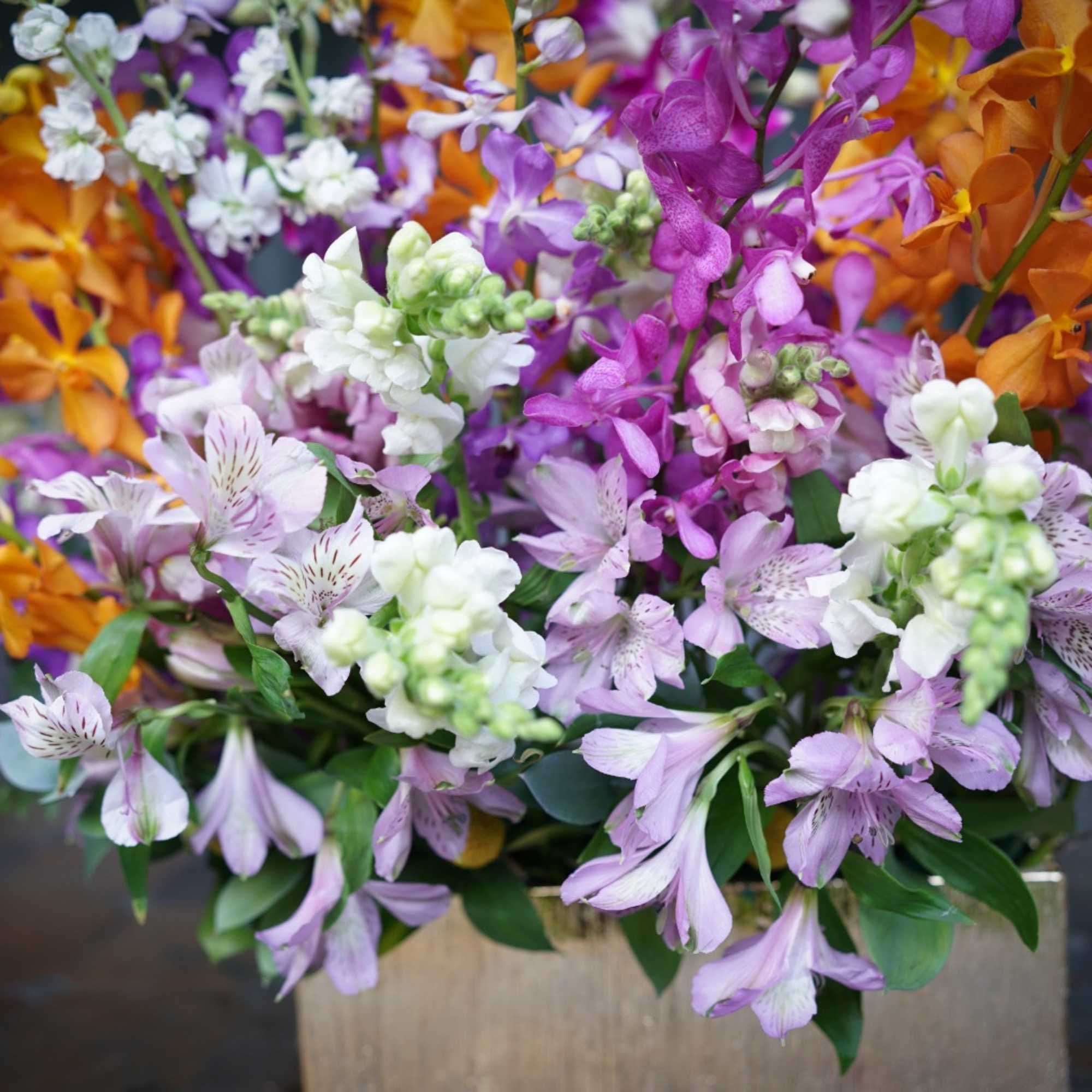 Mixed bouquet of purple, white, and orange flowers in a wooden container