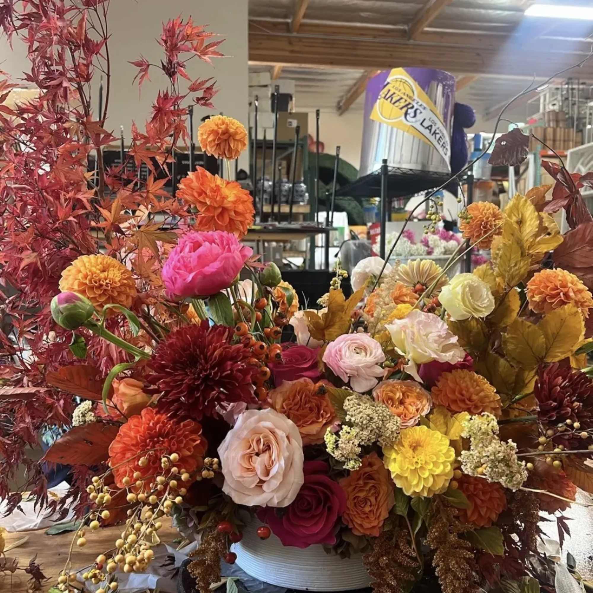 Large autumn floral arrangement with orange, pink, and yellow blooms in a white container