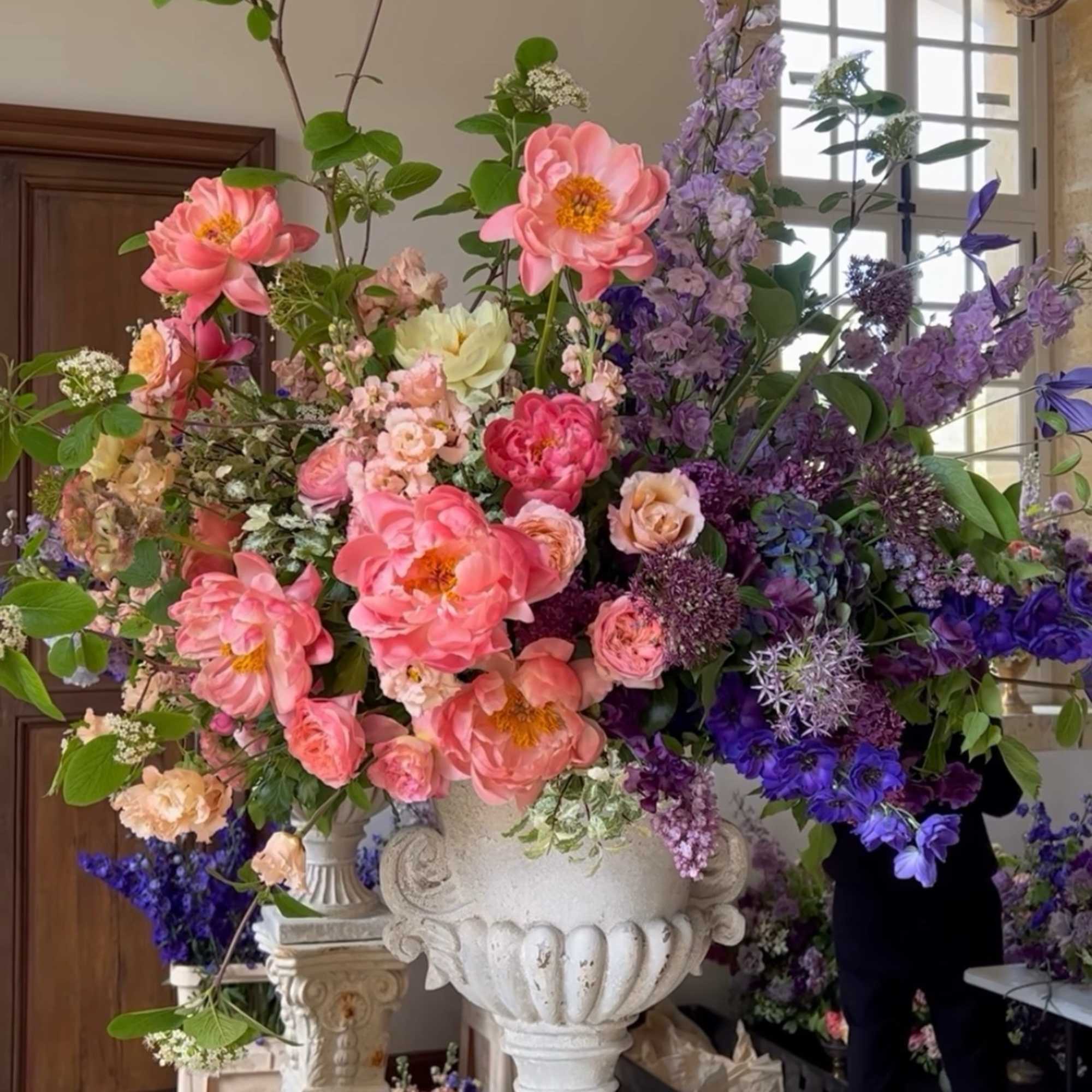Large floral arrangement with pink and purple blooms in a white urn