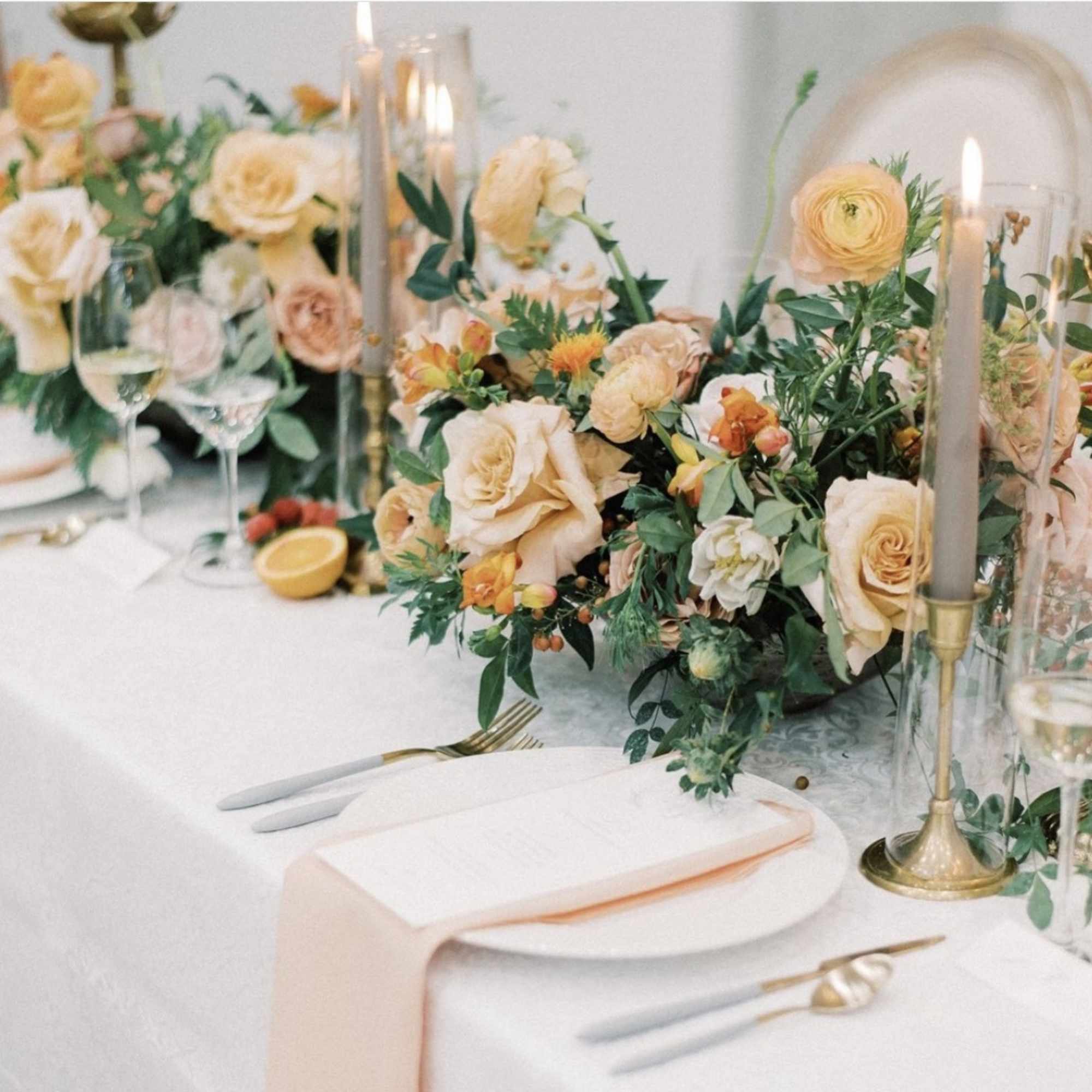 Peach and cream floral centerpiece with candles on a white table