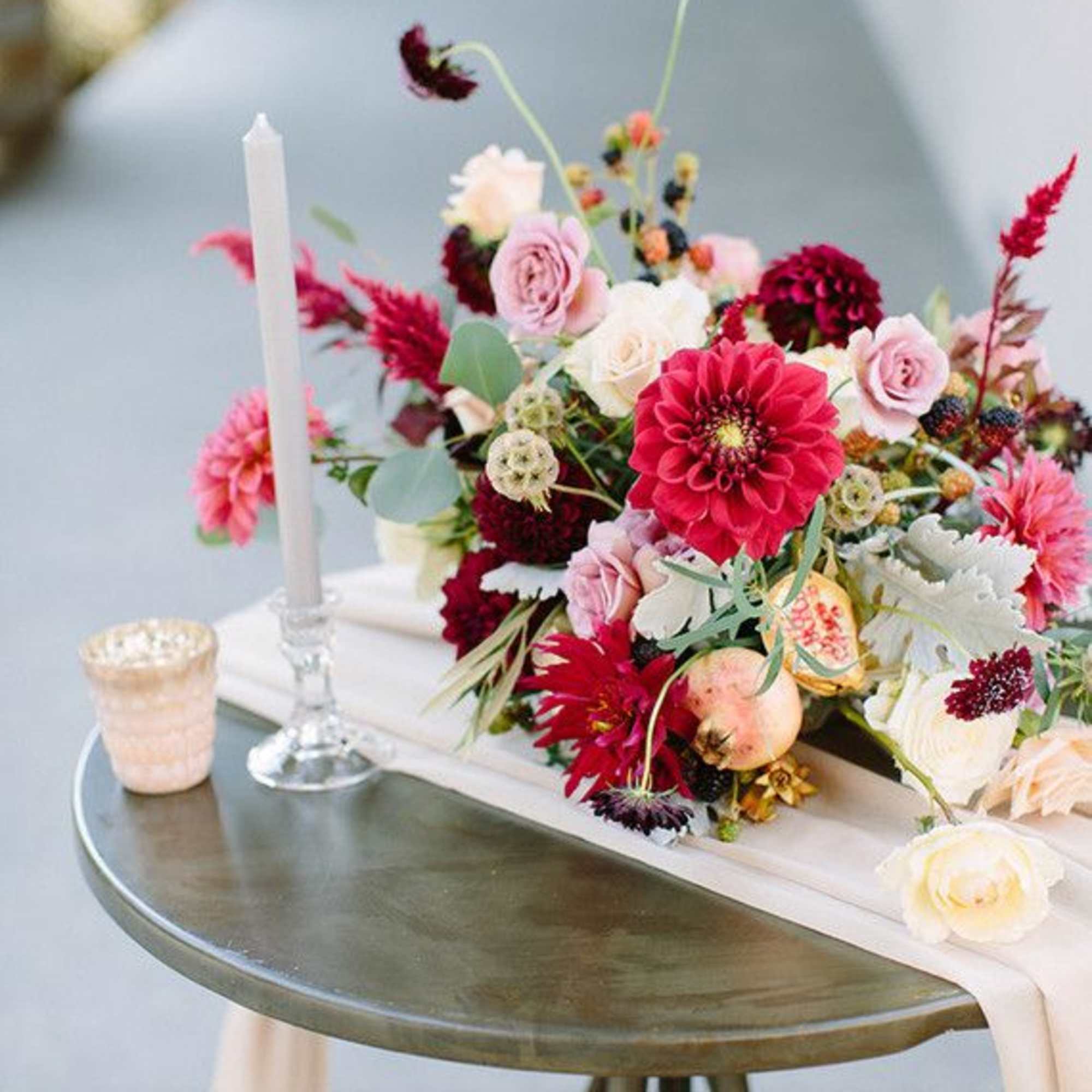 Low floral centerpiece with pink, white, and burgundy blooms beside a white candle