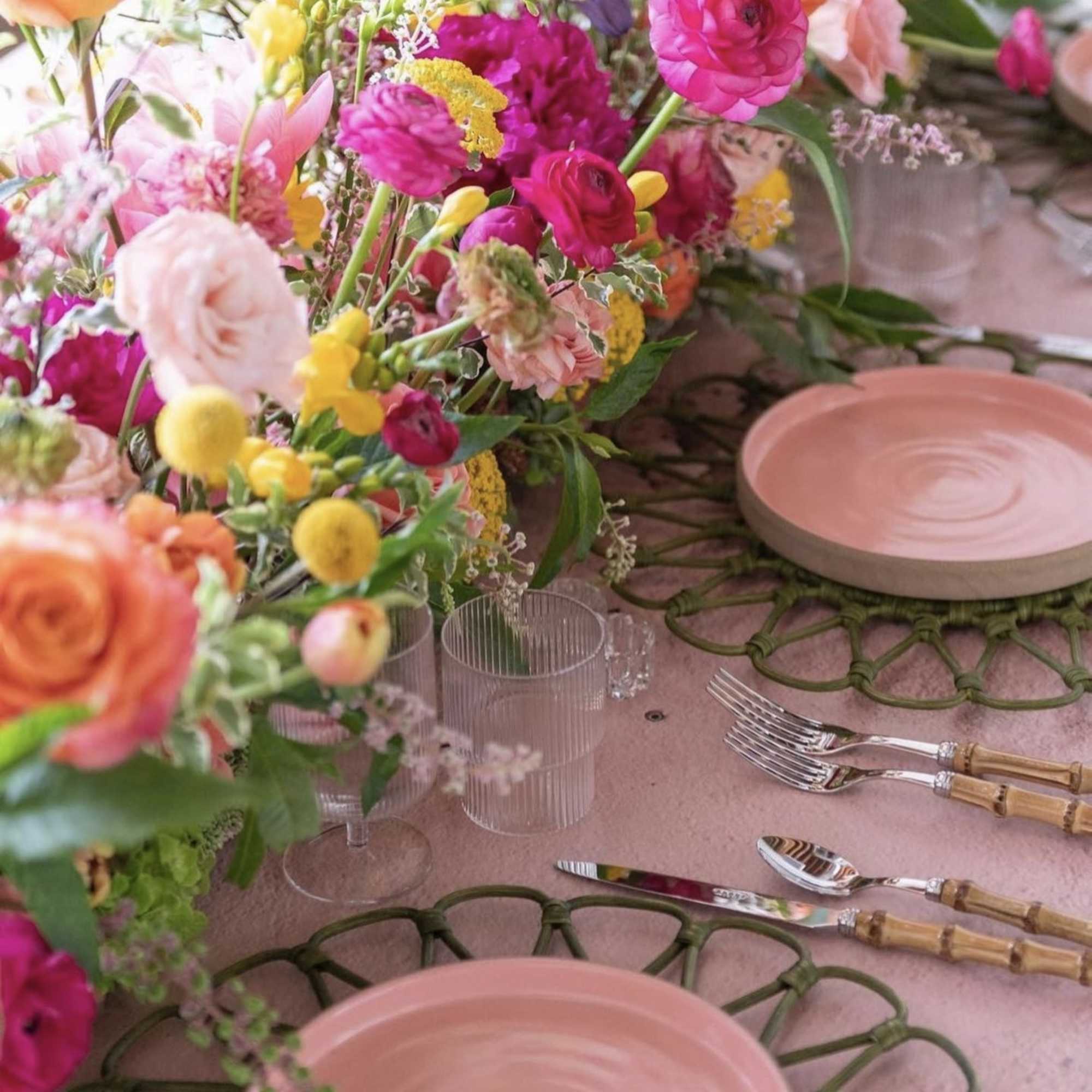 Colorful floral table centerpiece with pink plates and gold-handled flatware
