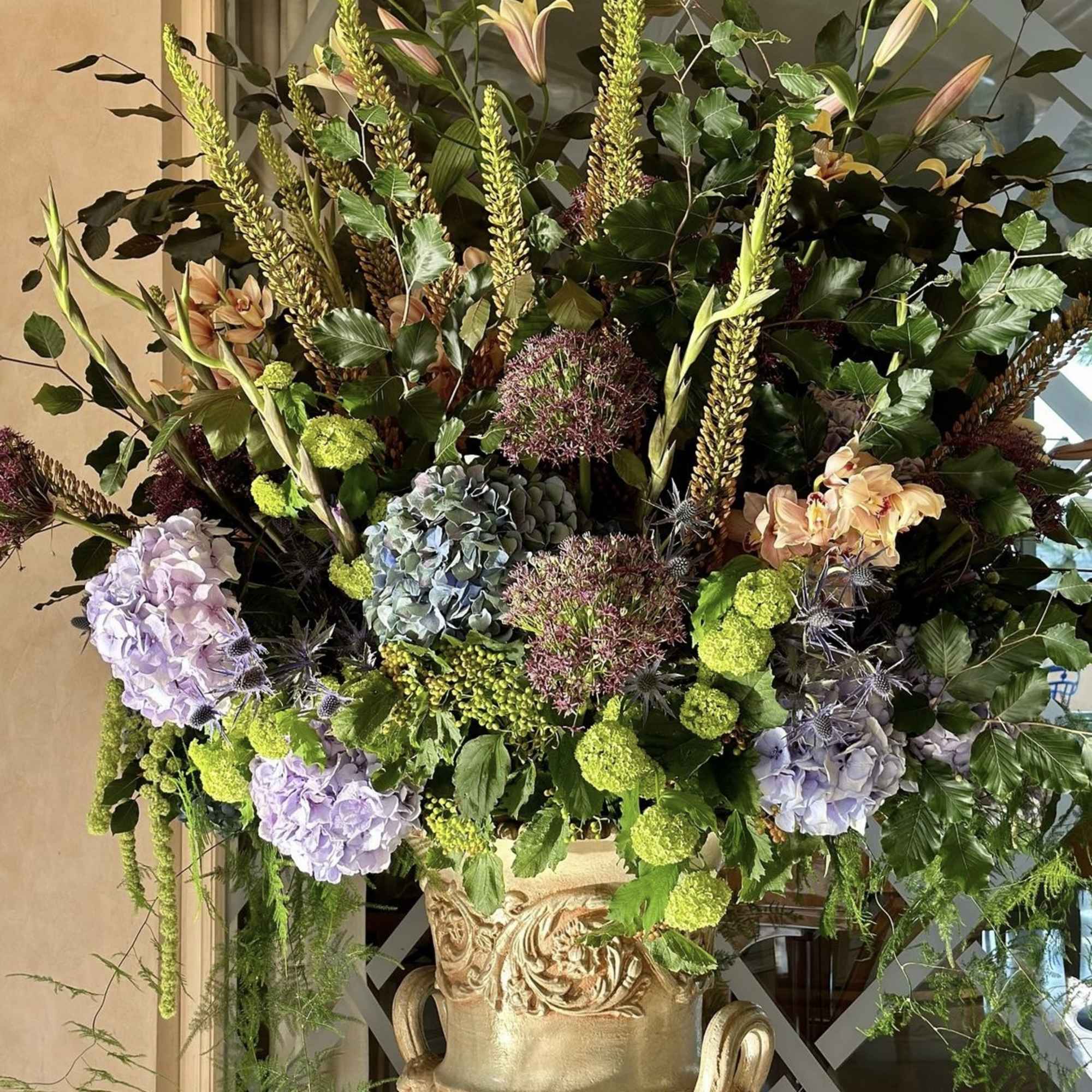 Large floral arrangement in an ornate gold urn with lilies and hydrangeas