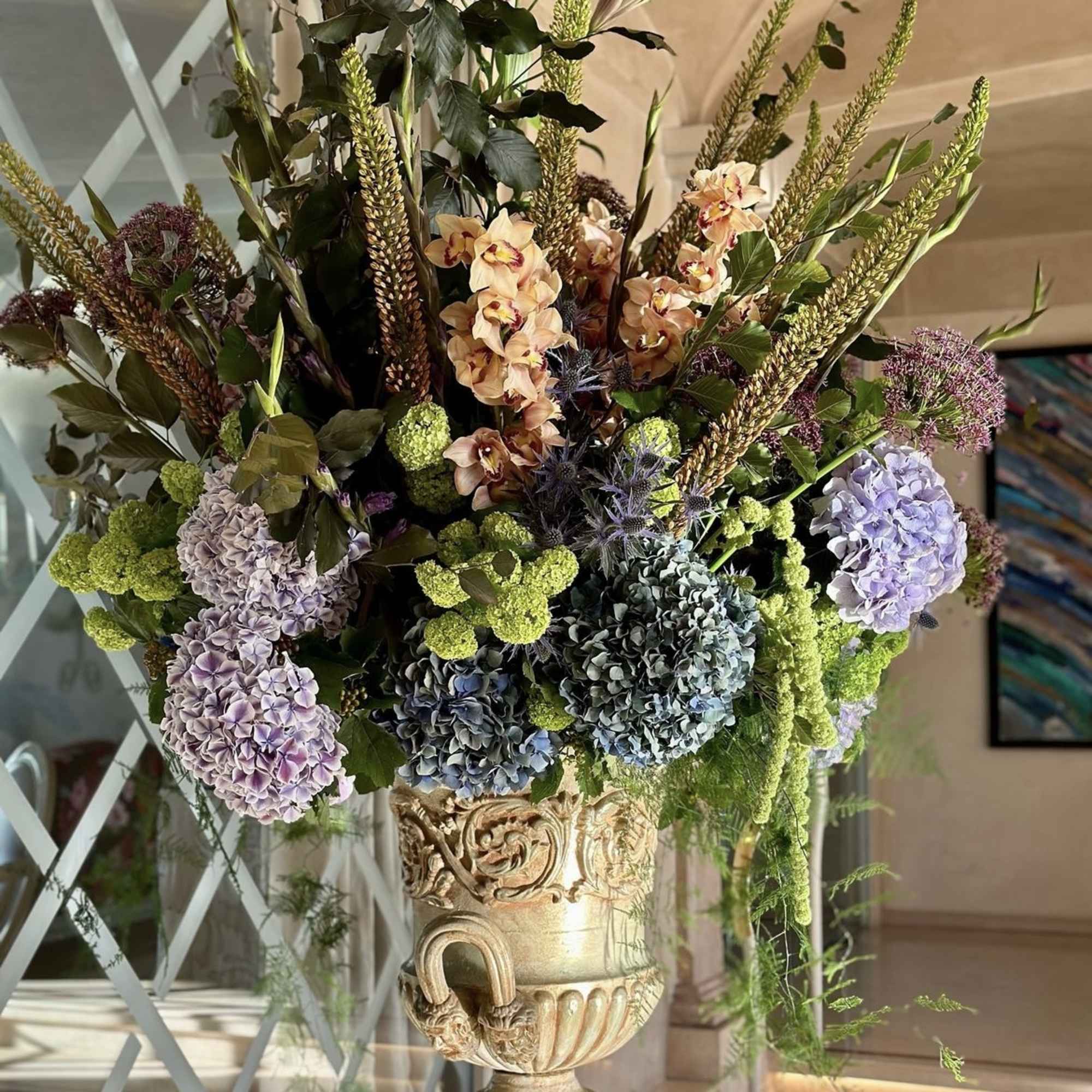 Tall floral arrangement in an ornate urn with hydrangeas and orchids