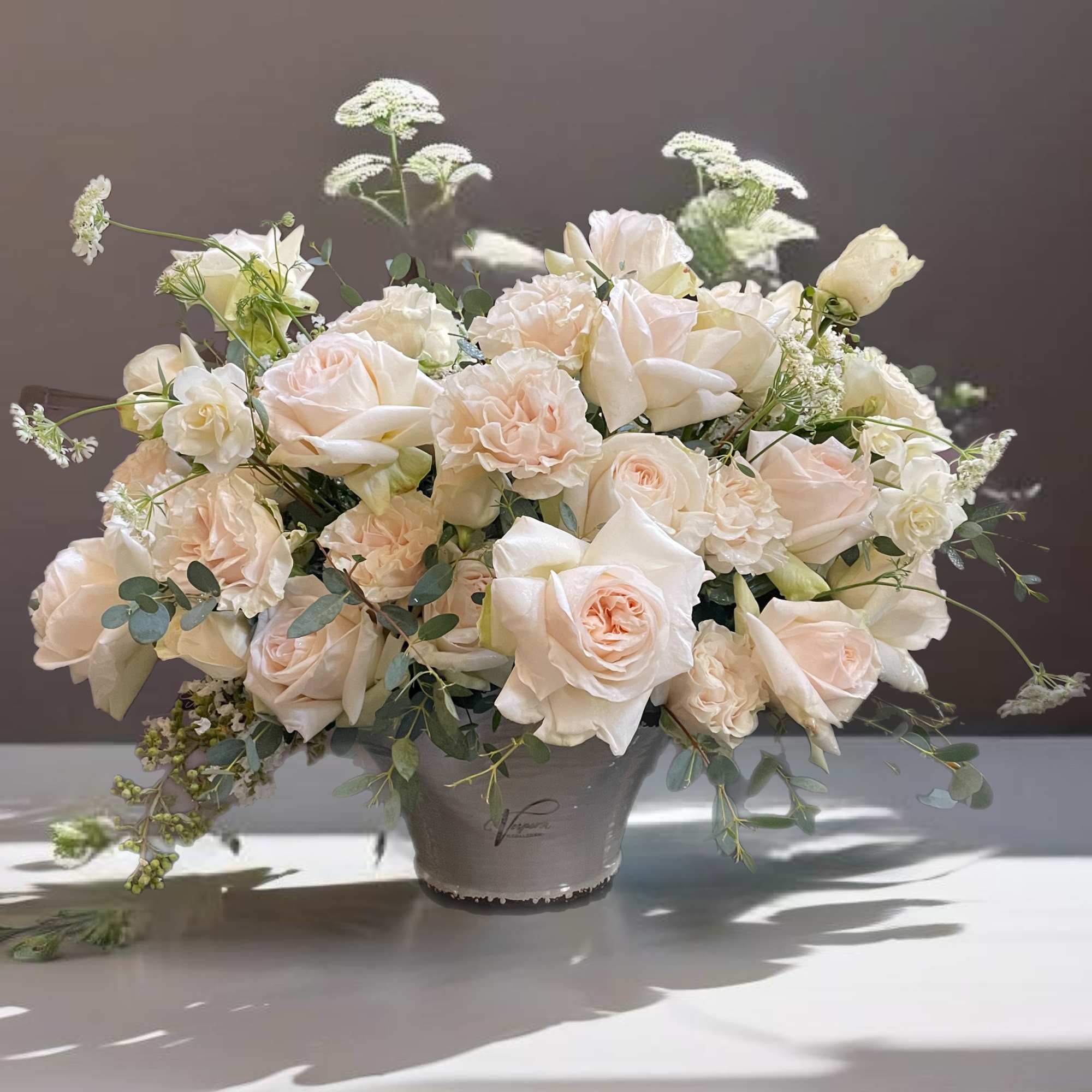 Cream roses arranged in a gray vase with airy greenery