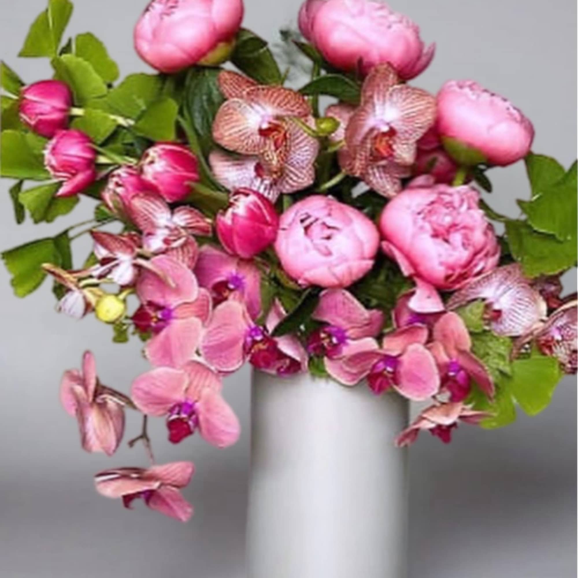 Pink peonies and orchids arranged in a white vase