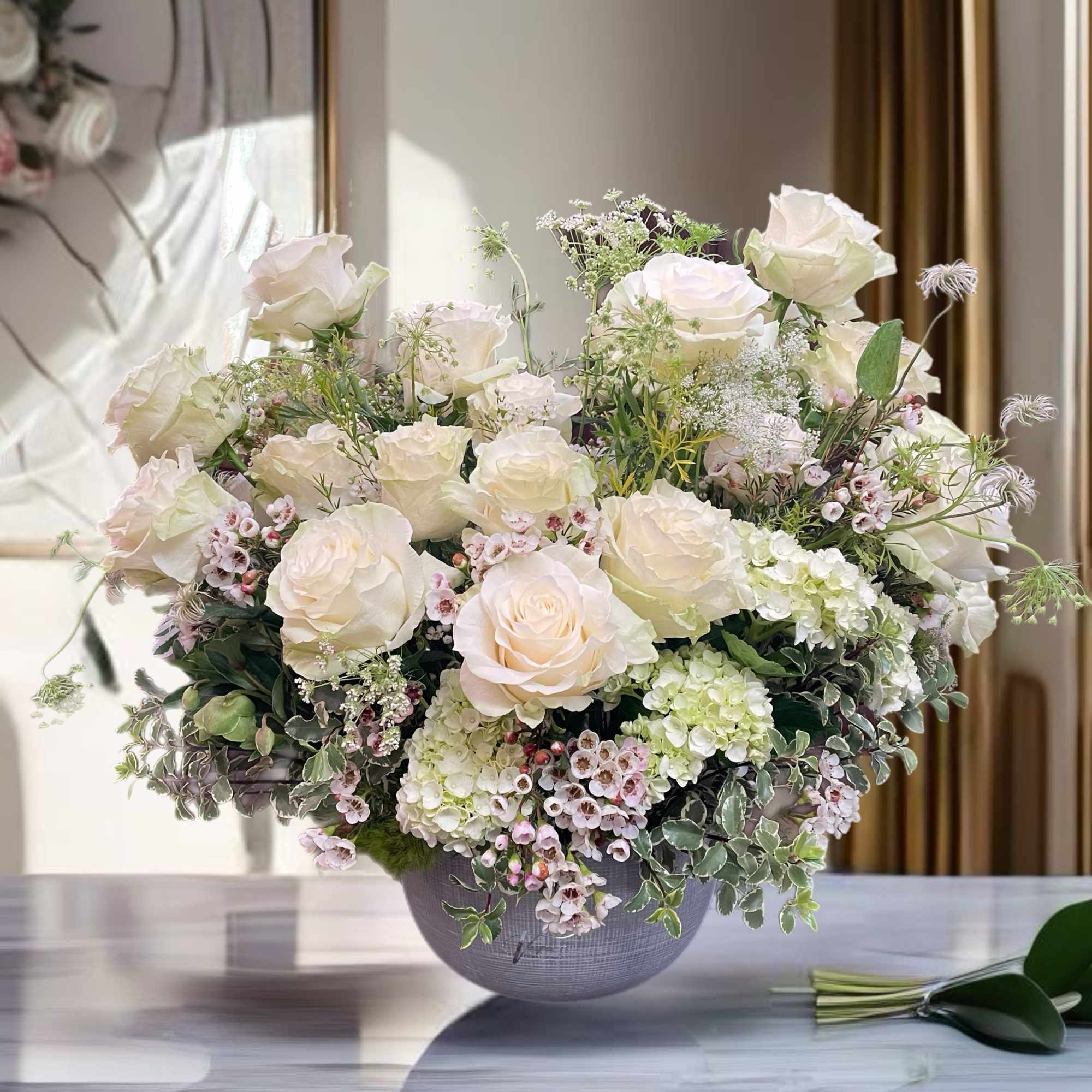Cream rose arrangement in a gray vase with small pink filler flowers