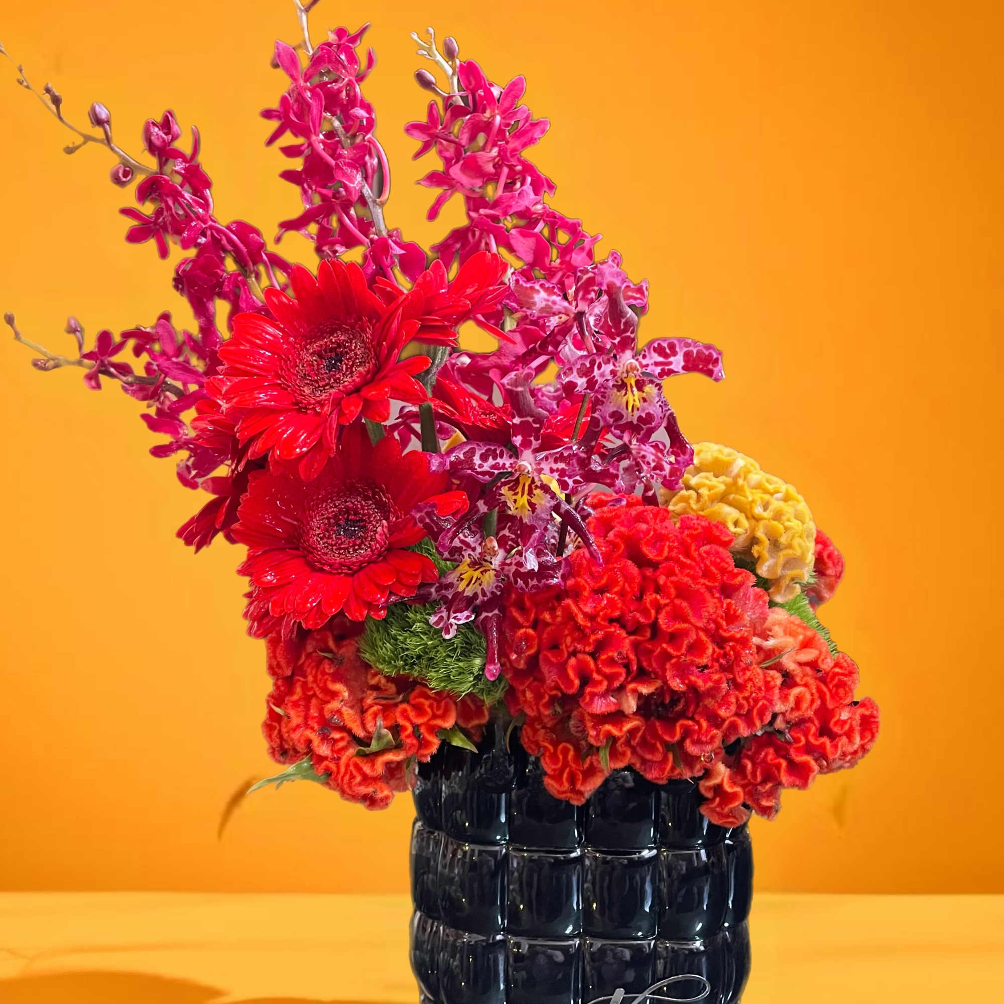 Bright mixed floral arrangement in a black vase against an orange background