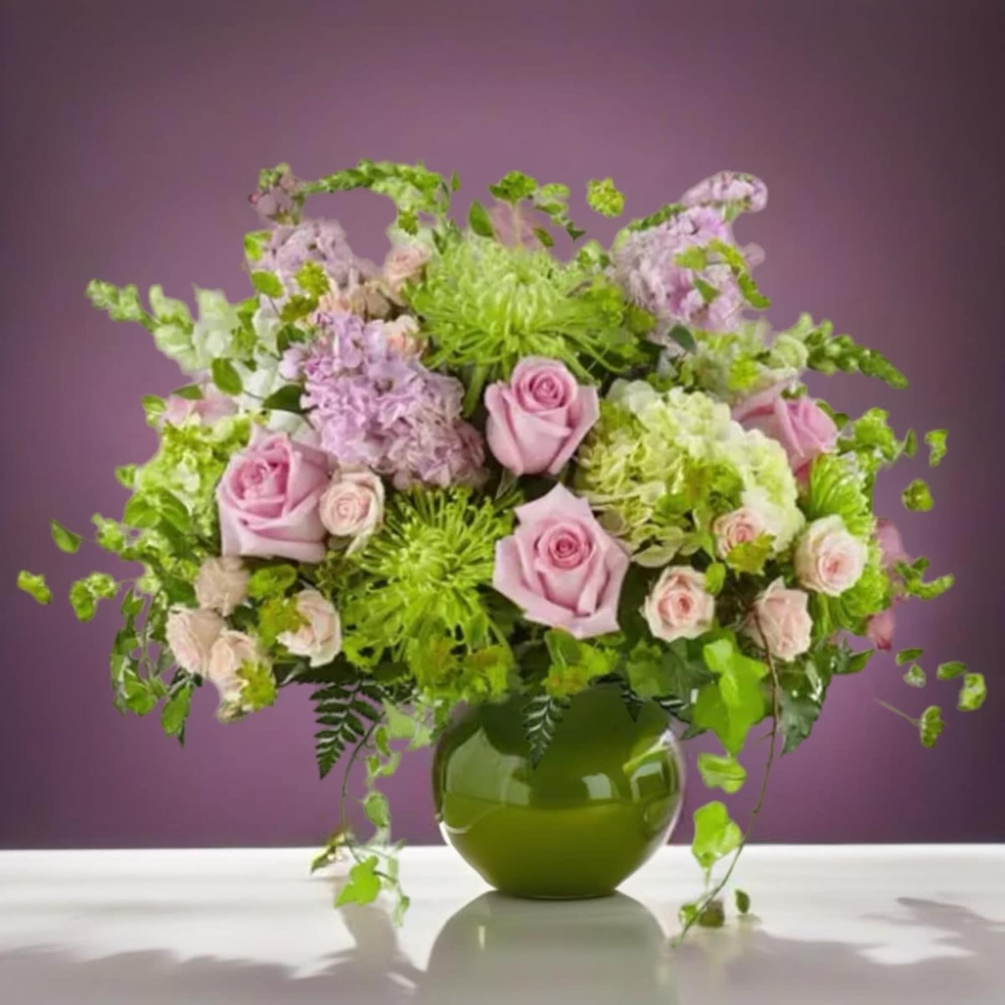 Pink roses and green blooms arranged in a round green vase