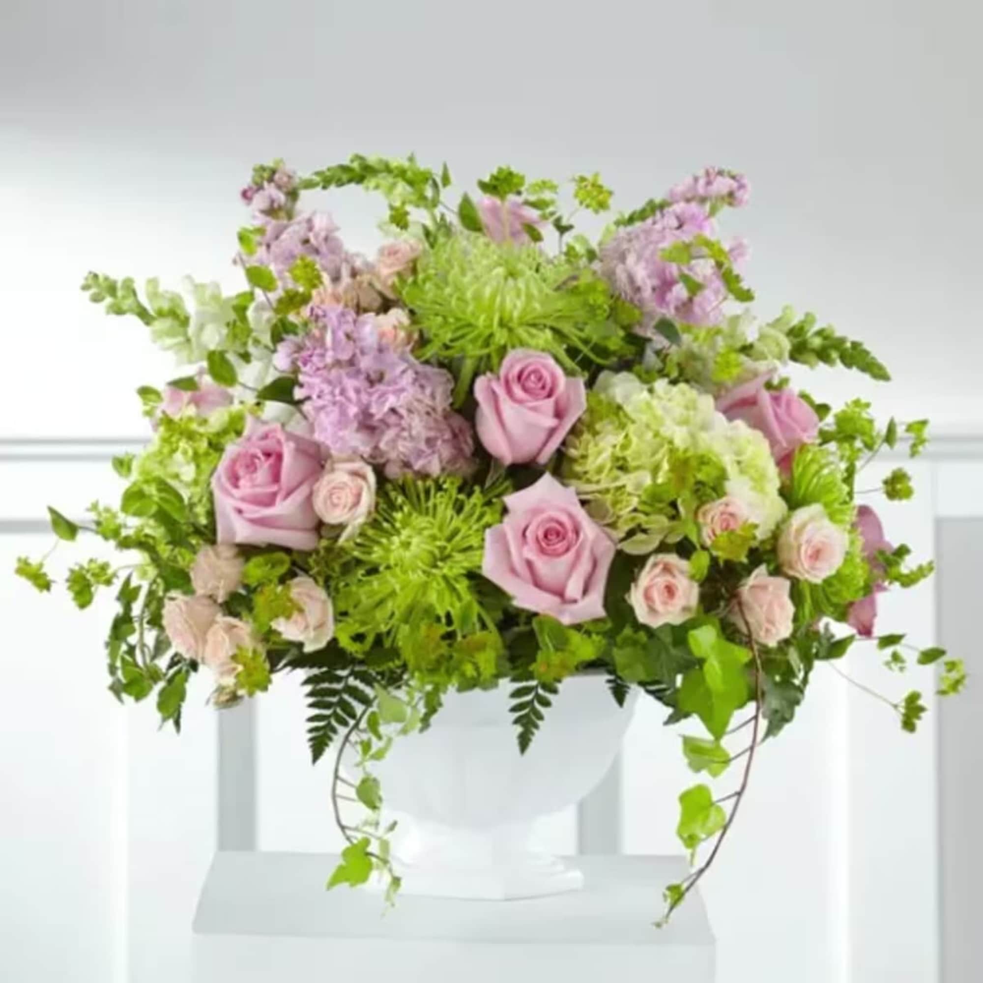 Pink roses and lavender blooms in a white vase with trailing greenery
