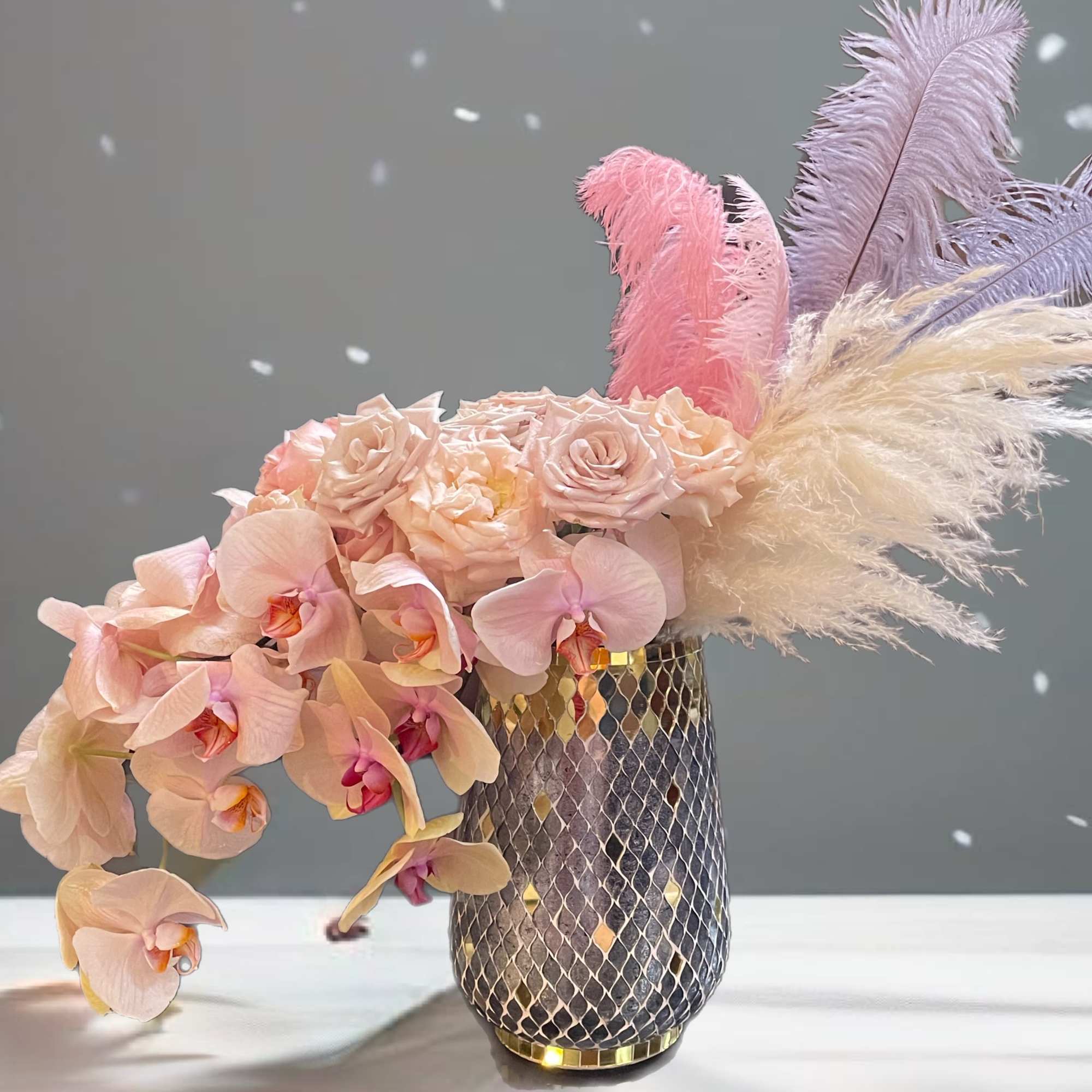 Pink orchids and roses in a patterned vase with pastel feathers