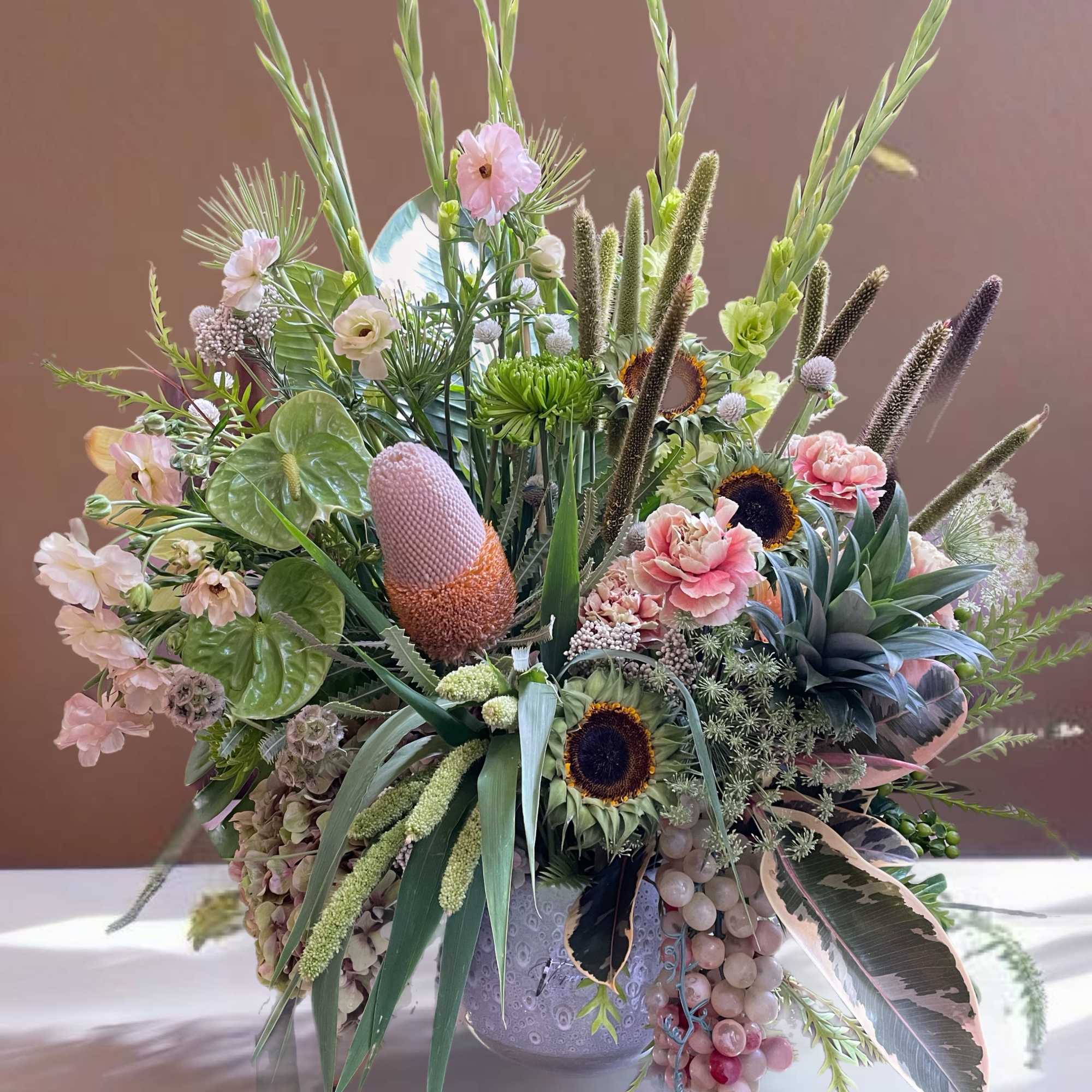 Large mixed floral arrangement with pink blooms and tall green spikes in a decorative vase