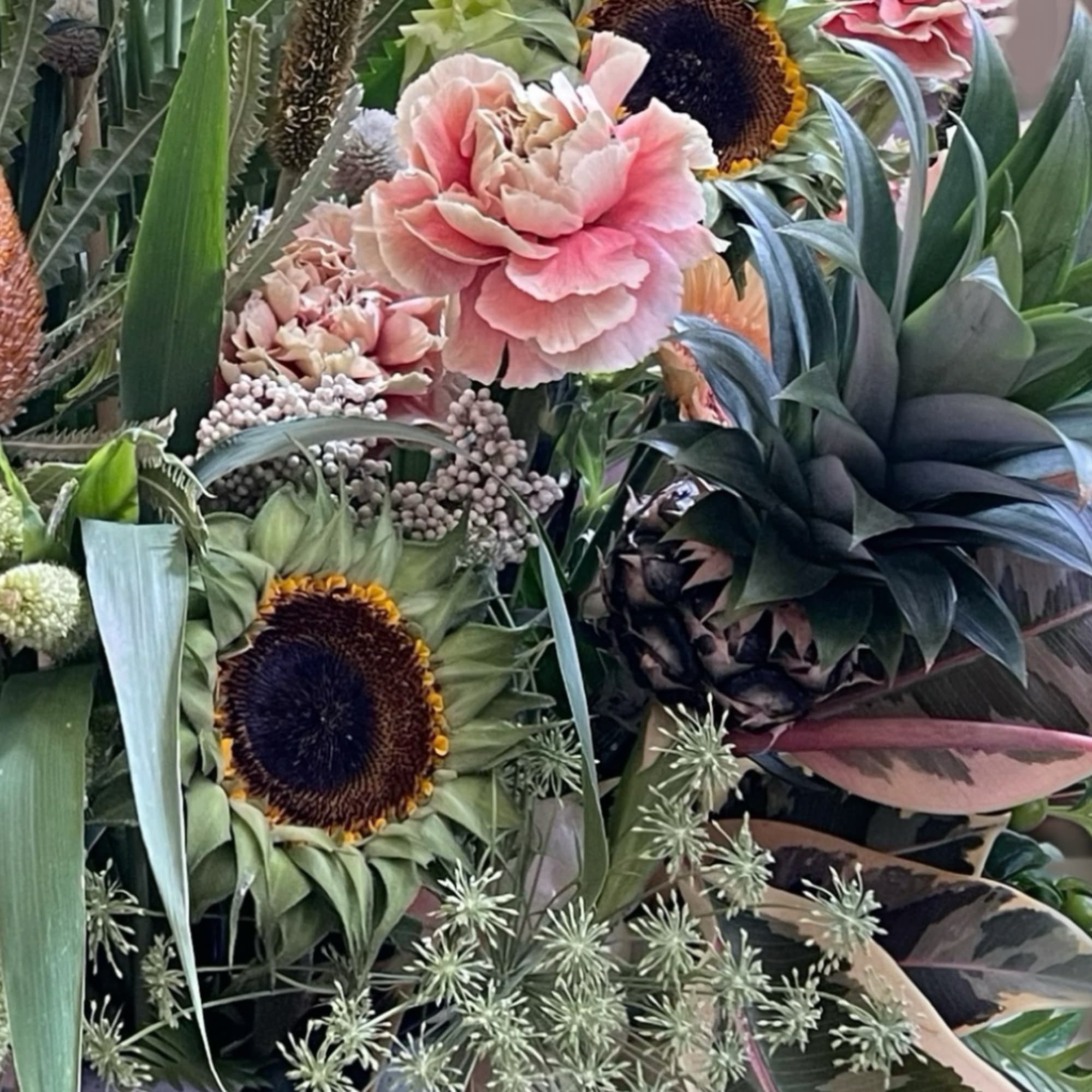 Mixed bouquet with sunflowers, pink carnations, and tropical foliage in a vase