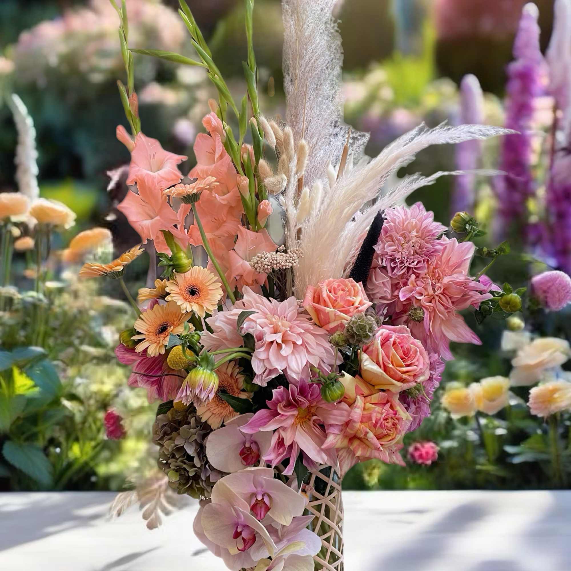 Pink and peach floral arrangement in a lattice vase with tall pampas grass