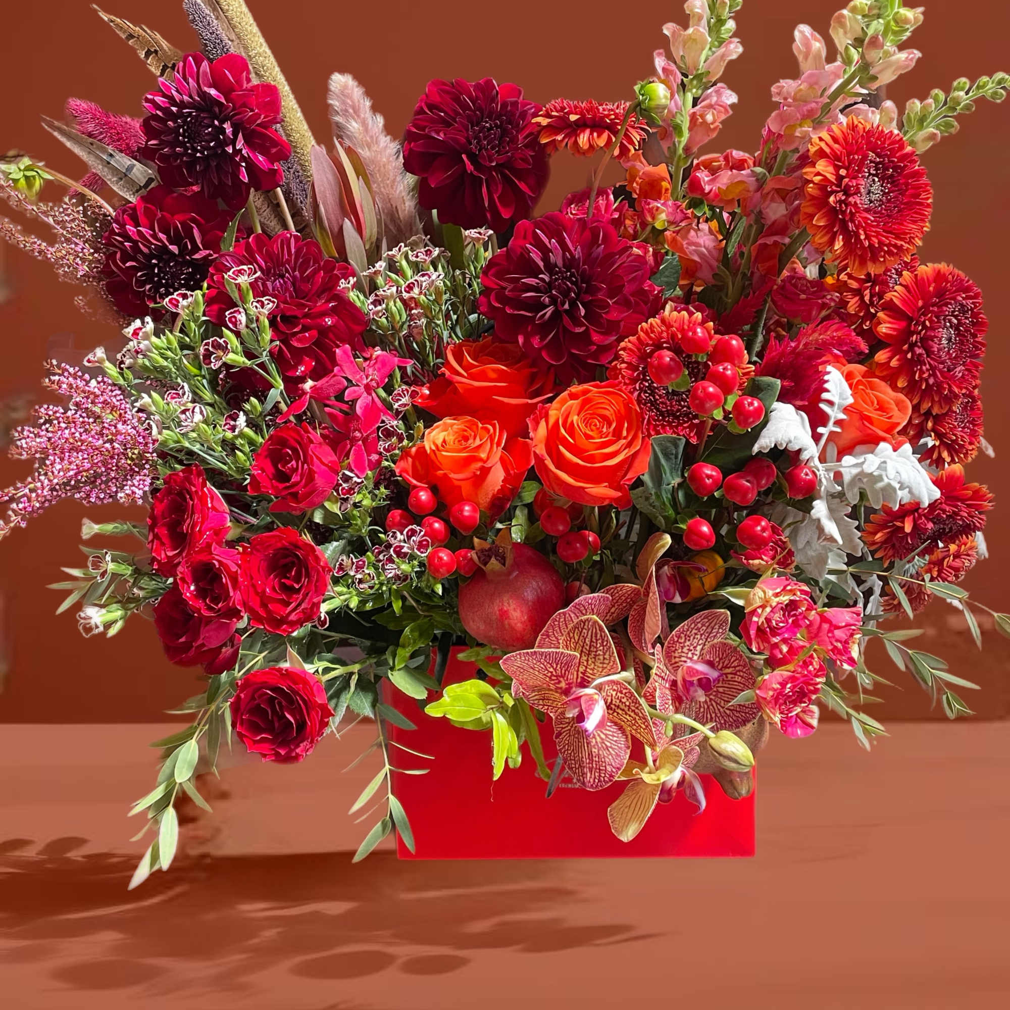 Red and orange floral arrangement in a red box with orchids and roses