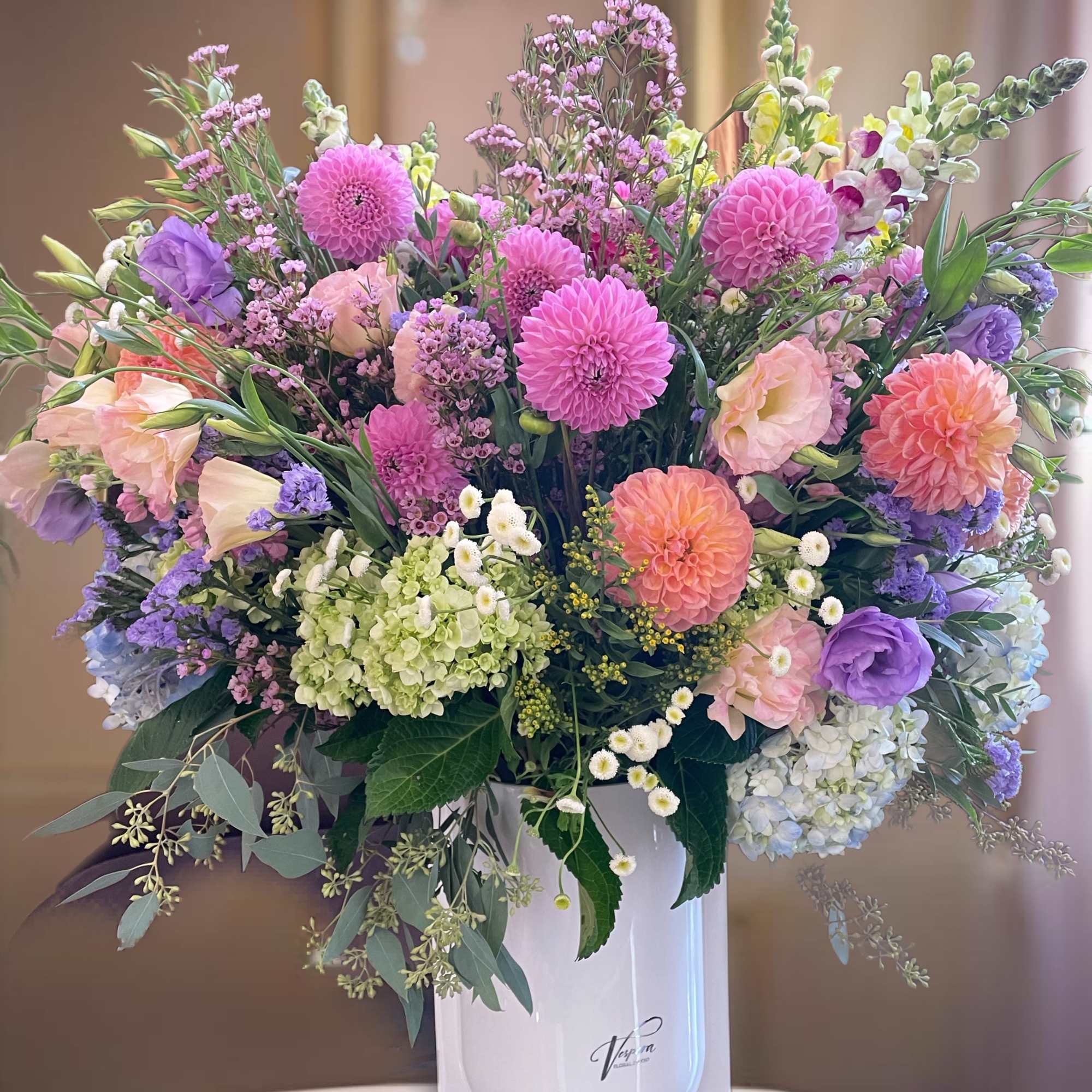 Large pastel bouquet in a white vase with pink, purple, peach, and green blooms