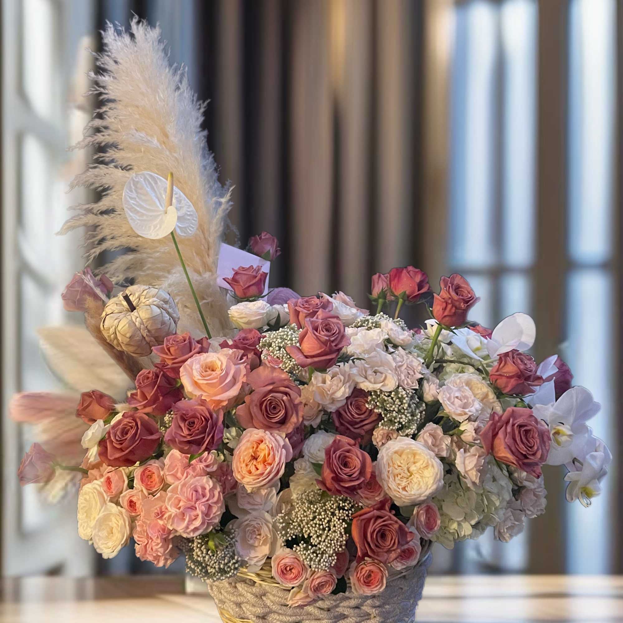 Basket arrangement of pink and white roses with pampas grass and orchids