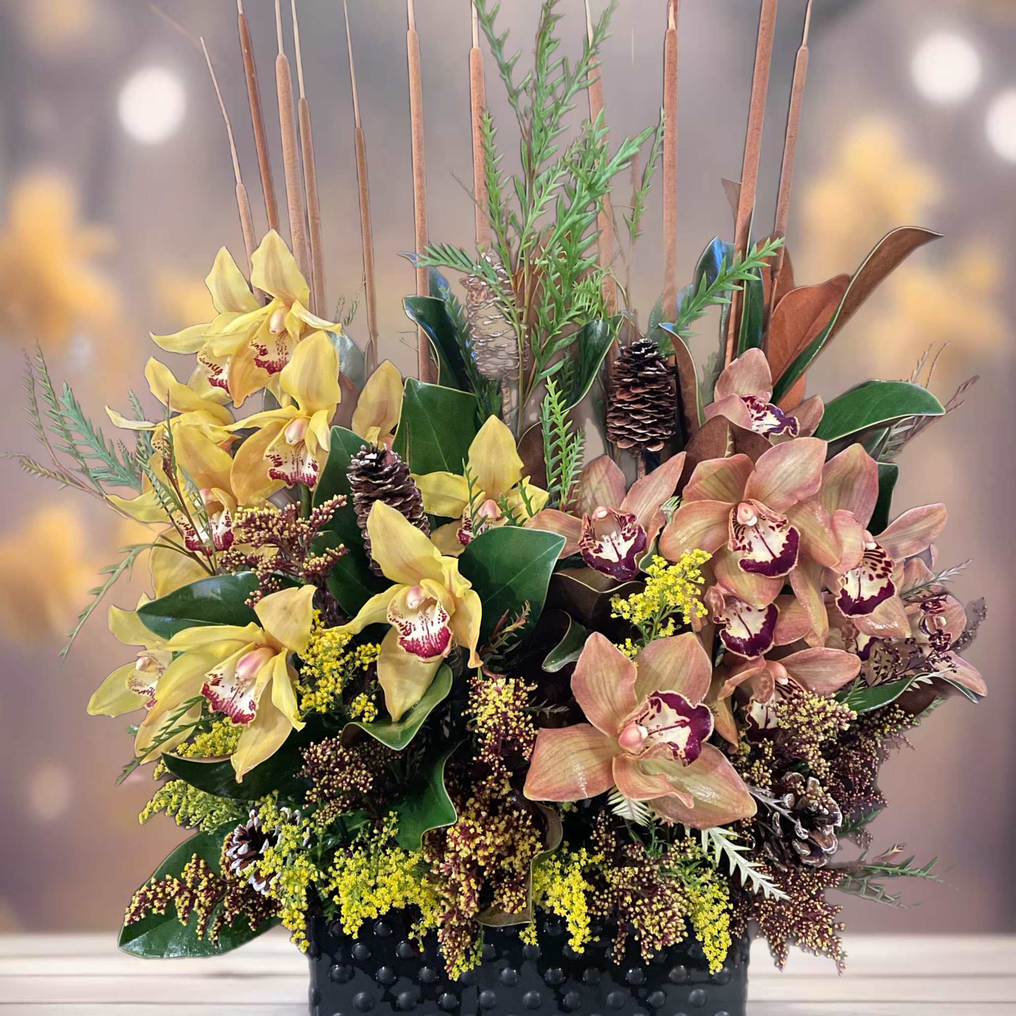 Arrangement of yellow and peach orchids in a black textured container