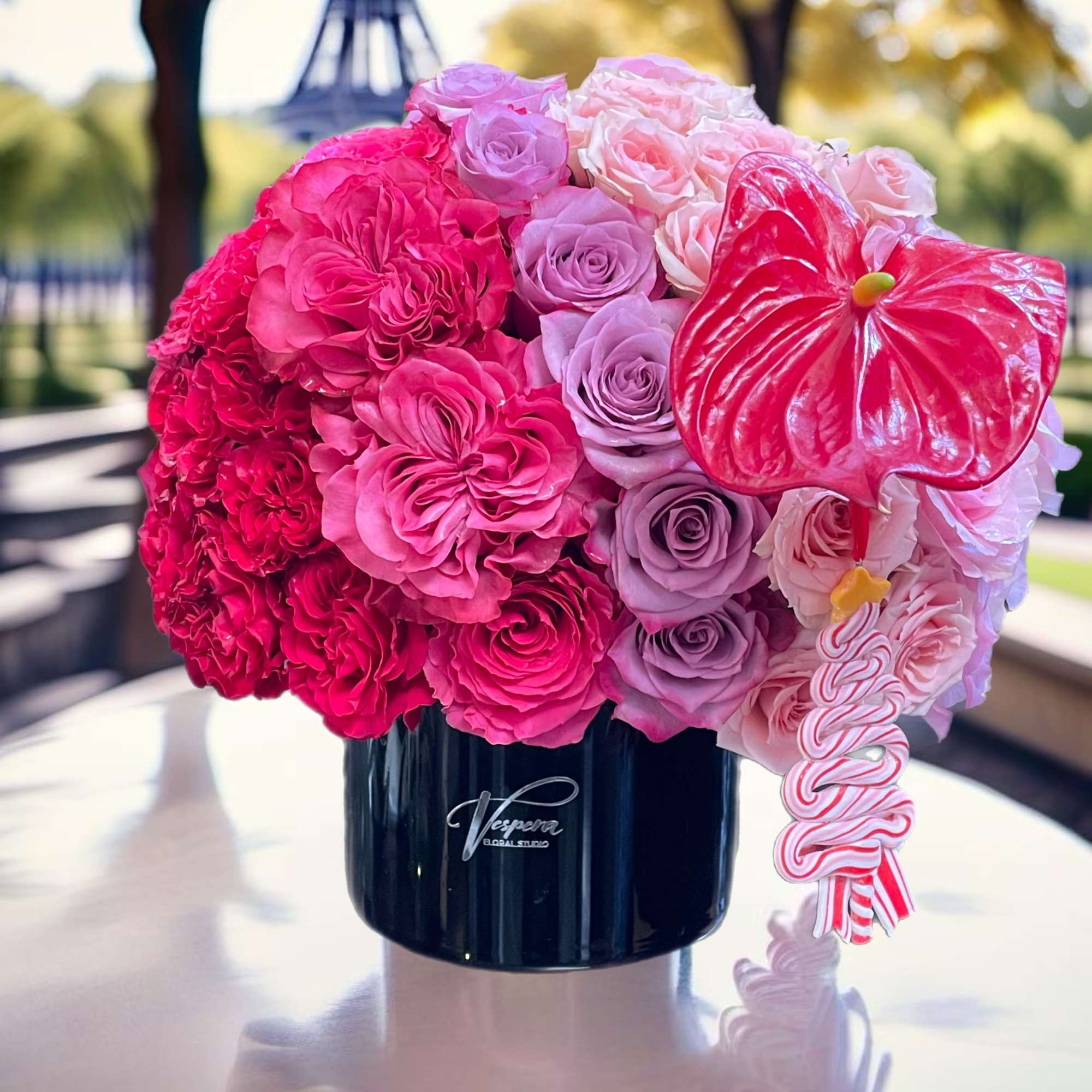 Pink and lavender rose arrangement in a black vase with a red heart accent