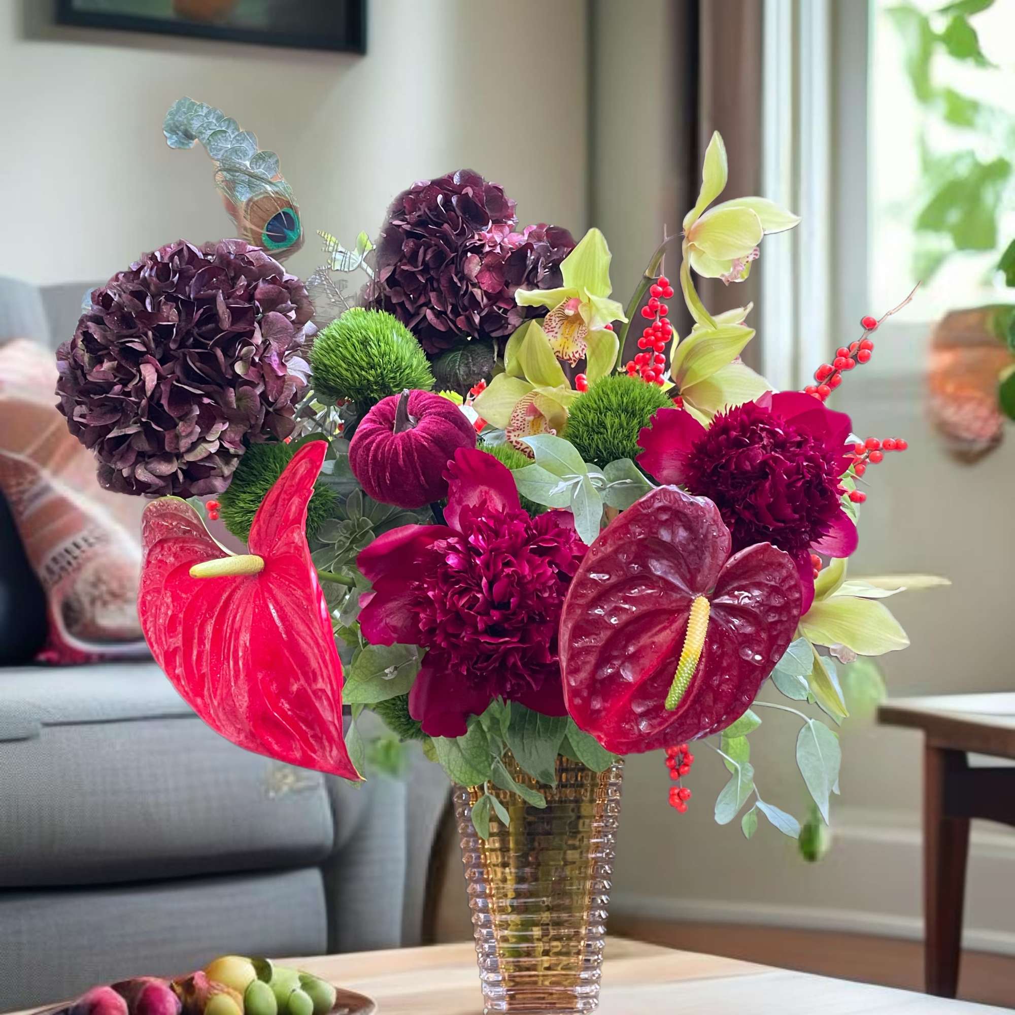 A colorful floral arrangement in a clear vase with purple blooms and red anthuriums.