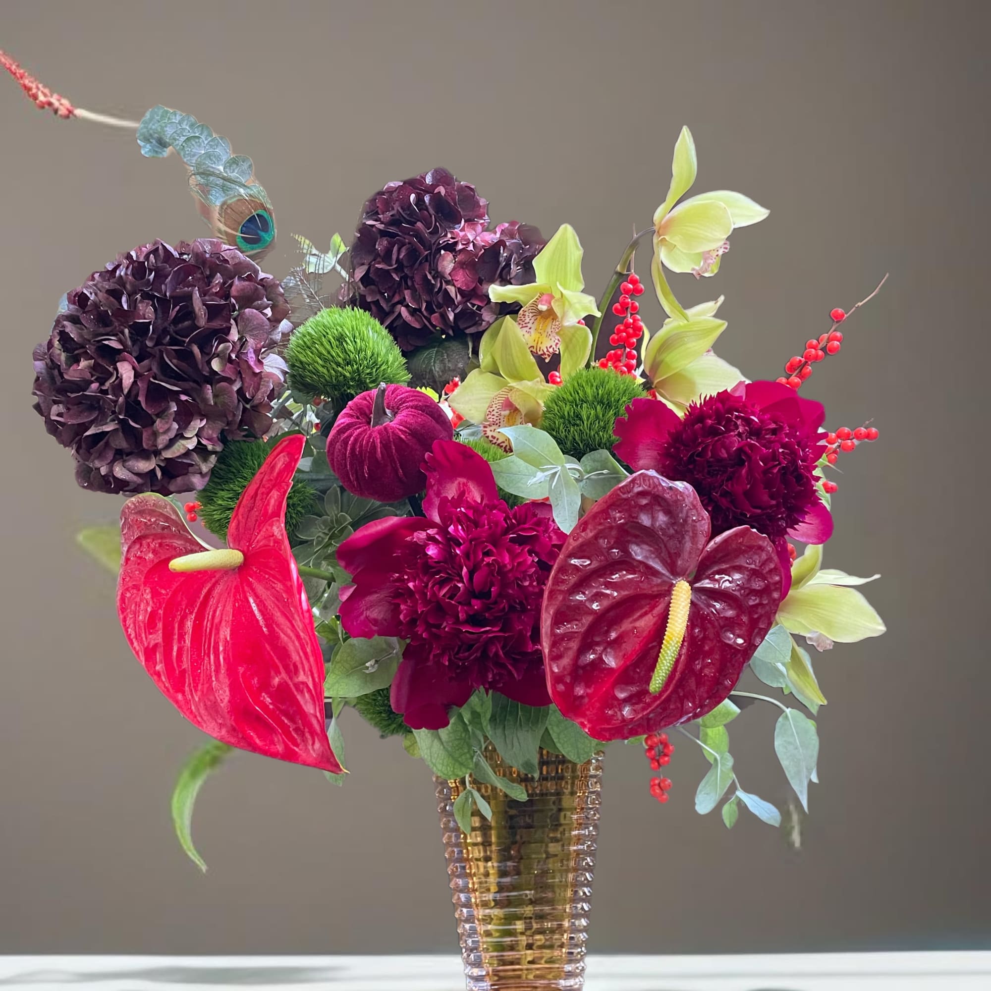 Mixed floral arrangement in a ribbed glass vase with red anthuriums and dark blooms