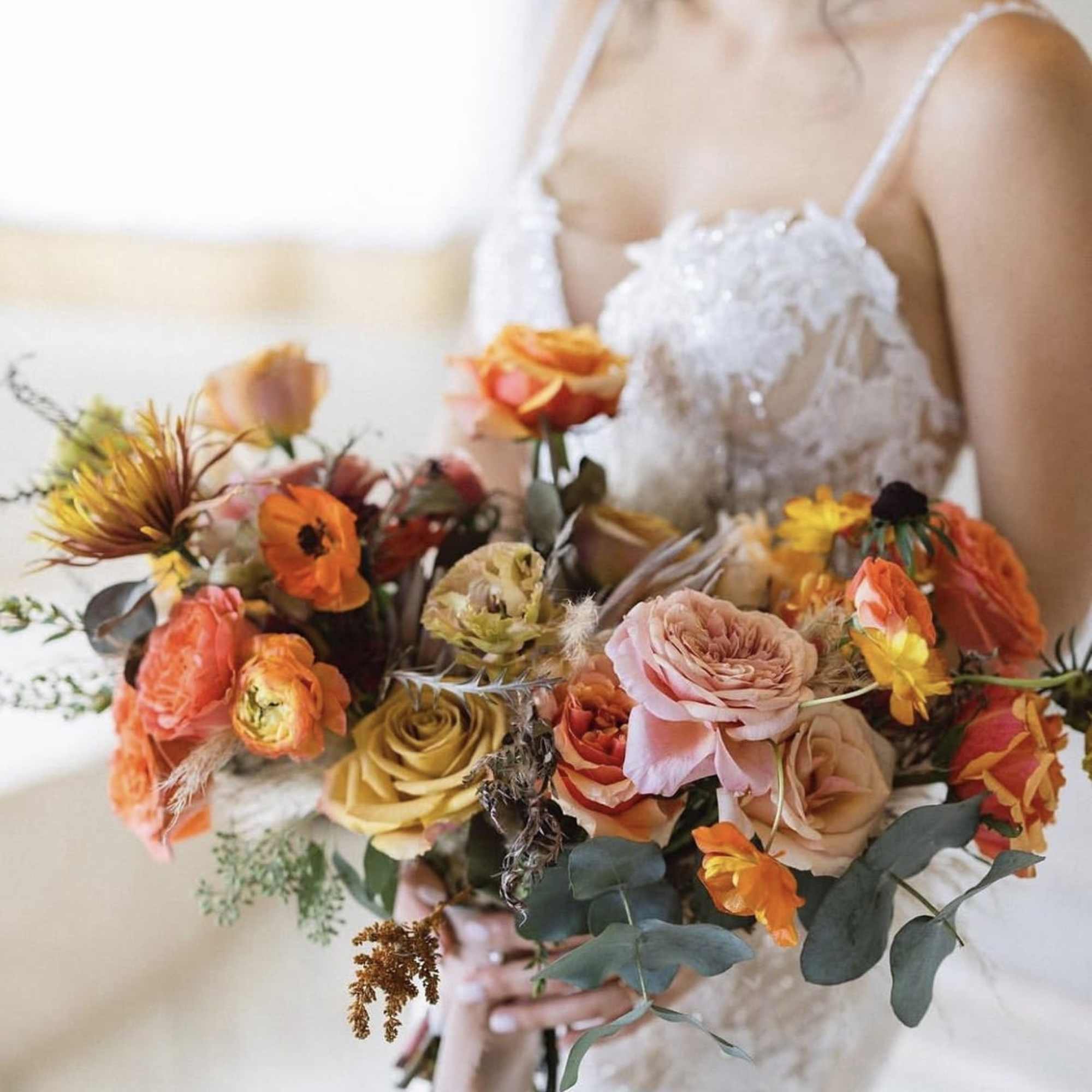 Bride holding a colorful bouquet of roses and orange blooms