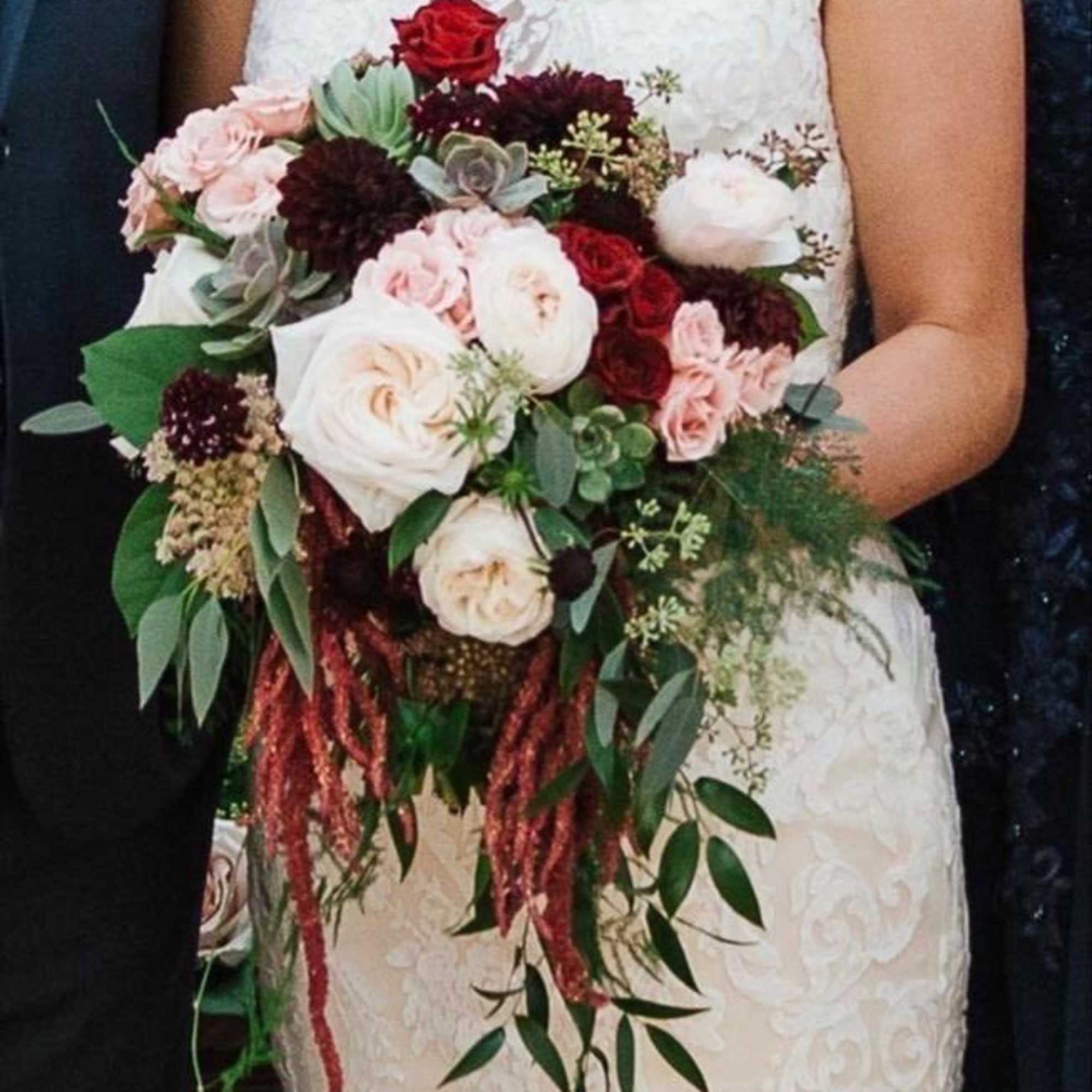 Bride holding a cascading bouquet of red, blush, and white flowers