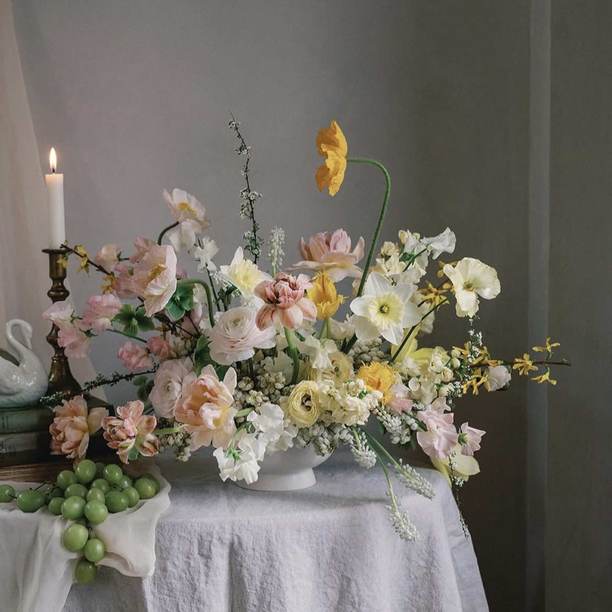 Pastel floral arrangement in a white vase with a lit candle nearby