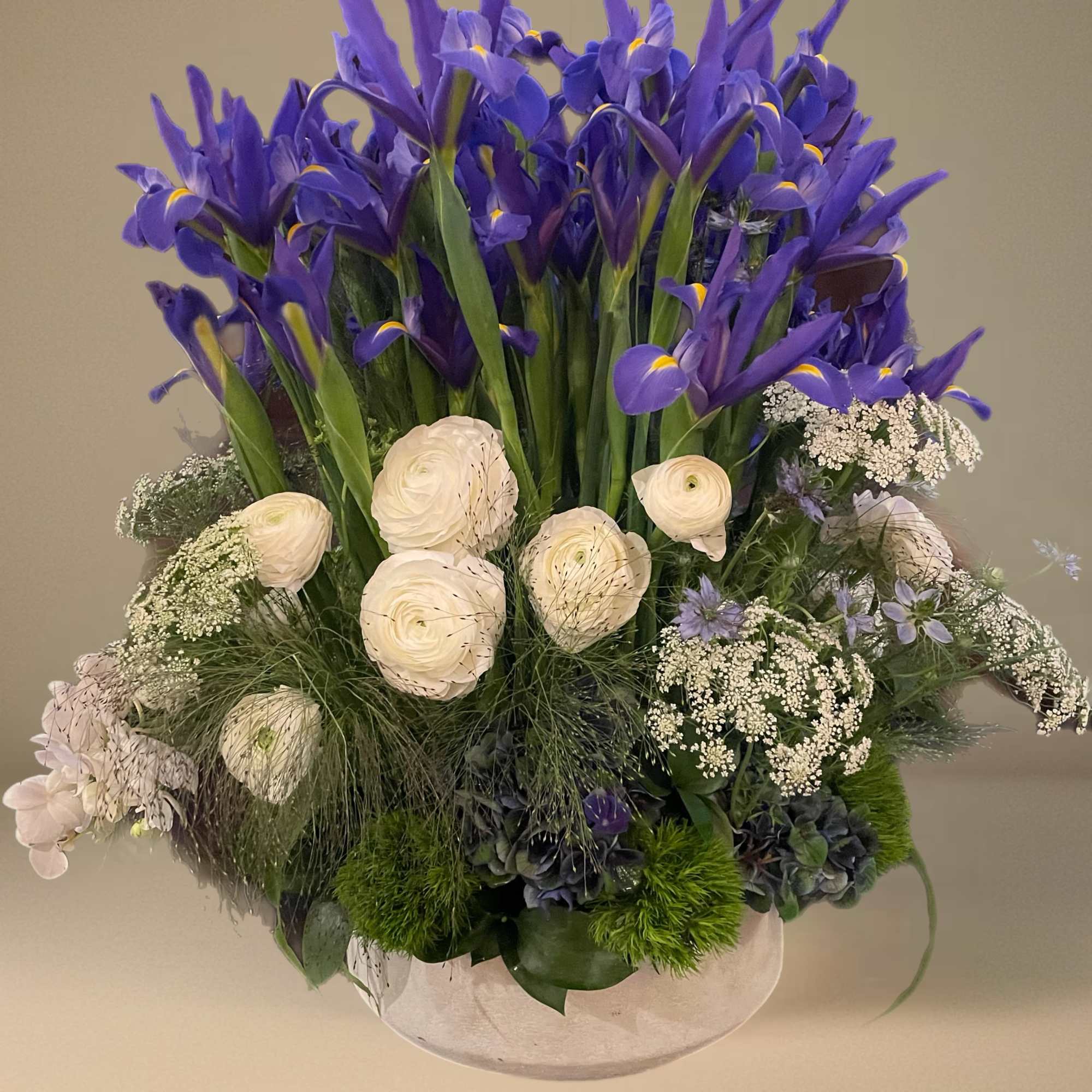 Purple iris and white ranunculus arranged in a low white bowl