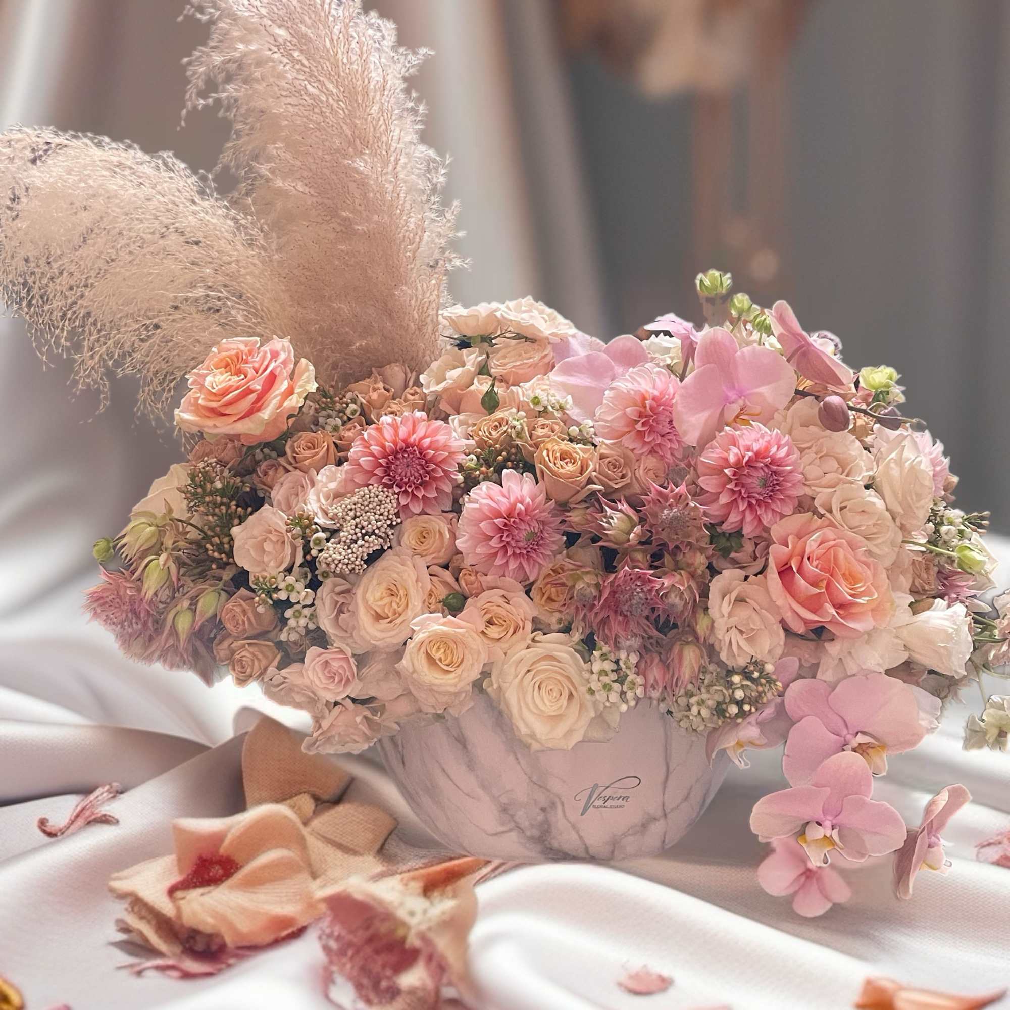 Pastel bouquet of roses, orchids, and dahlias in a marble vase