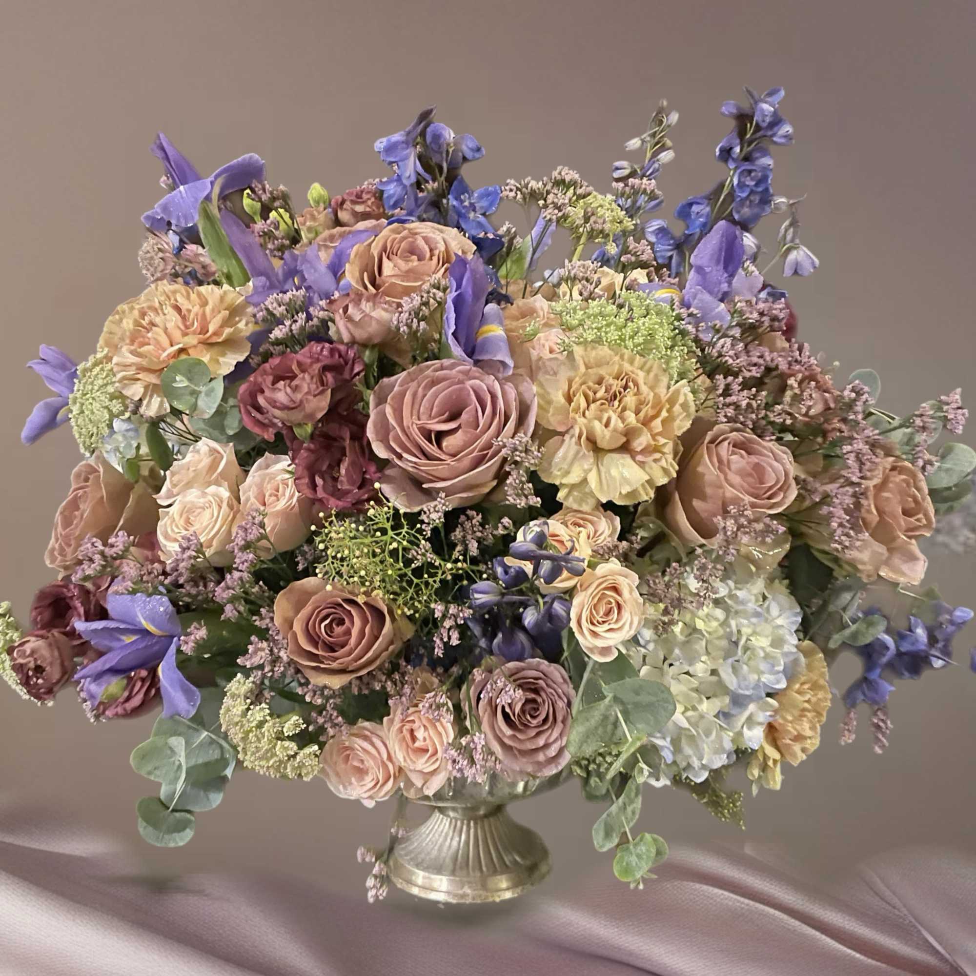 Large pastel bouquet of roses, carnations, and blue flowers in a silver vase