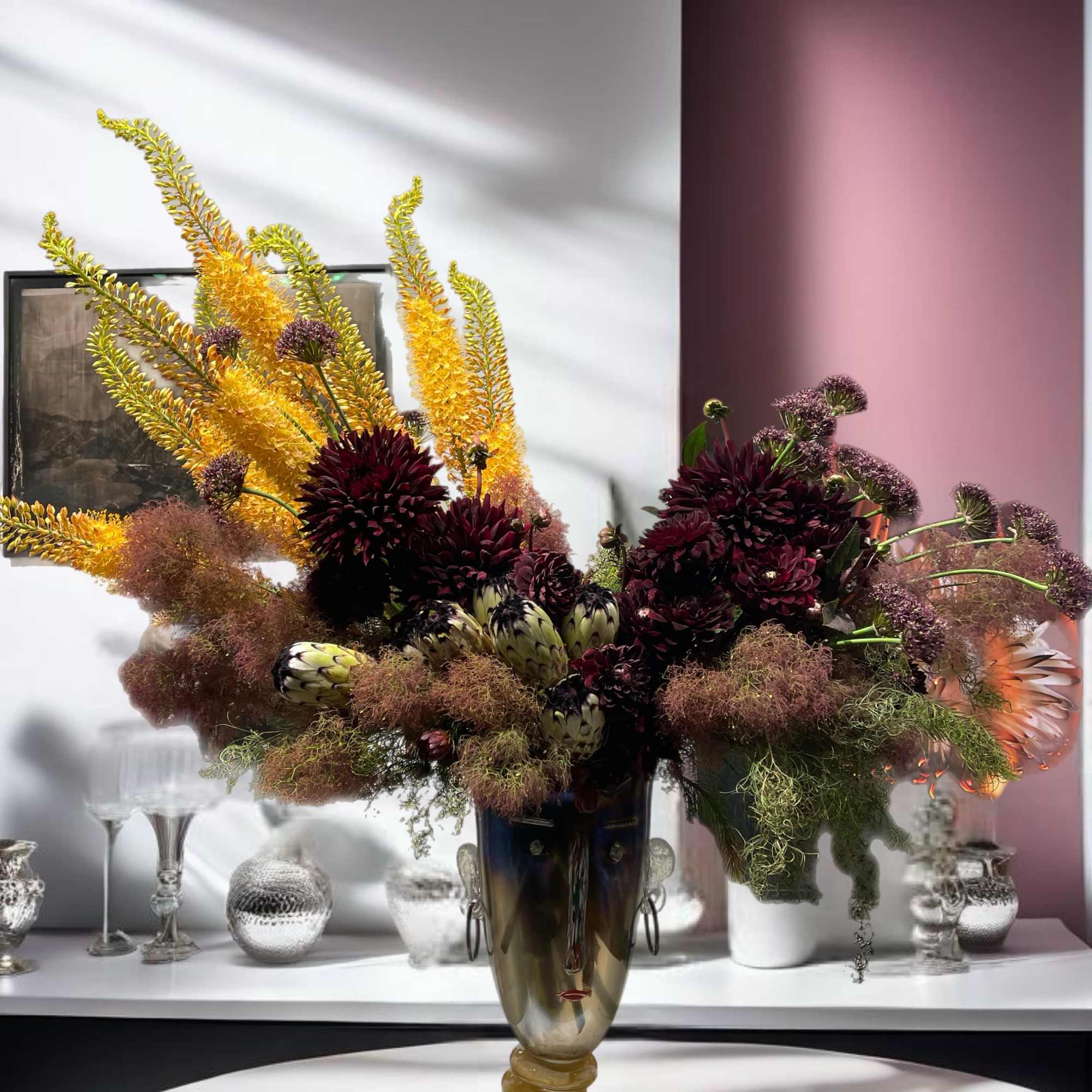 Large floral arrangement in a tall vase with dark burgundy and yellow blooms