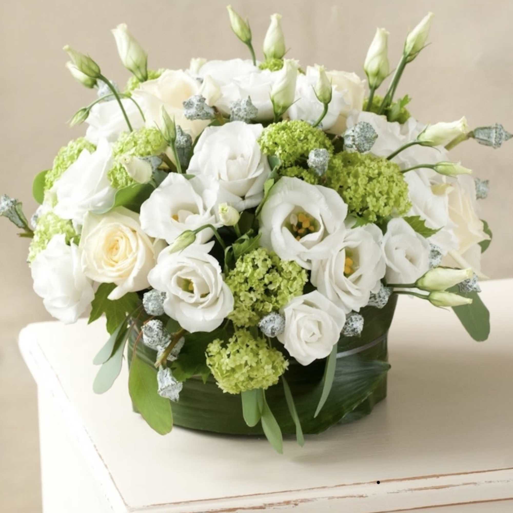 White roses and lisianthus arranged in a low round box