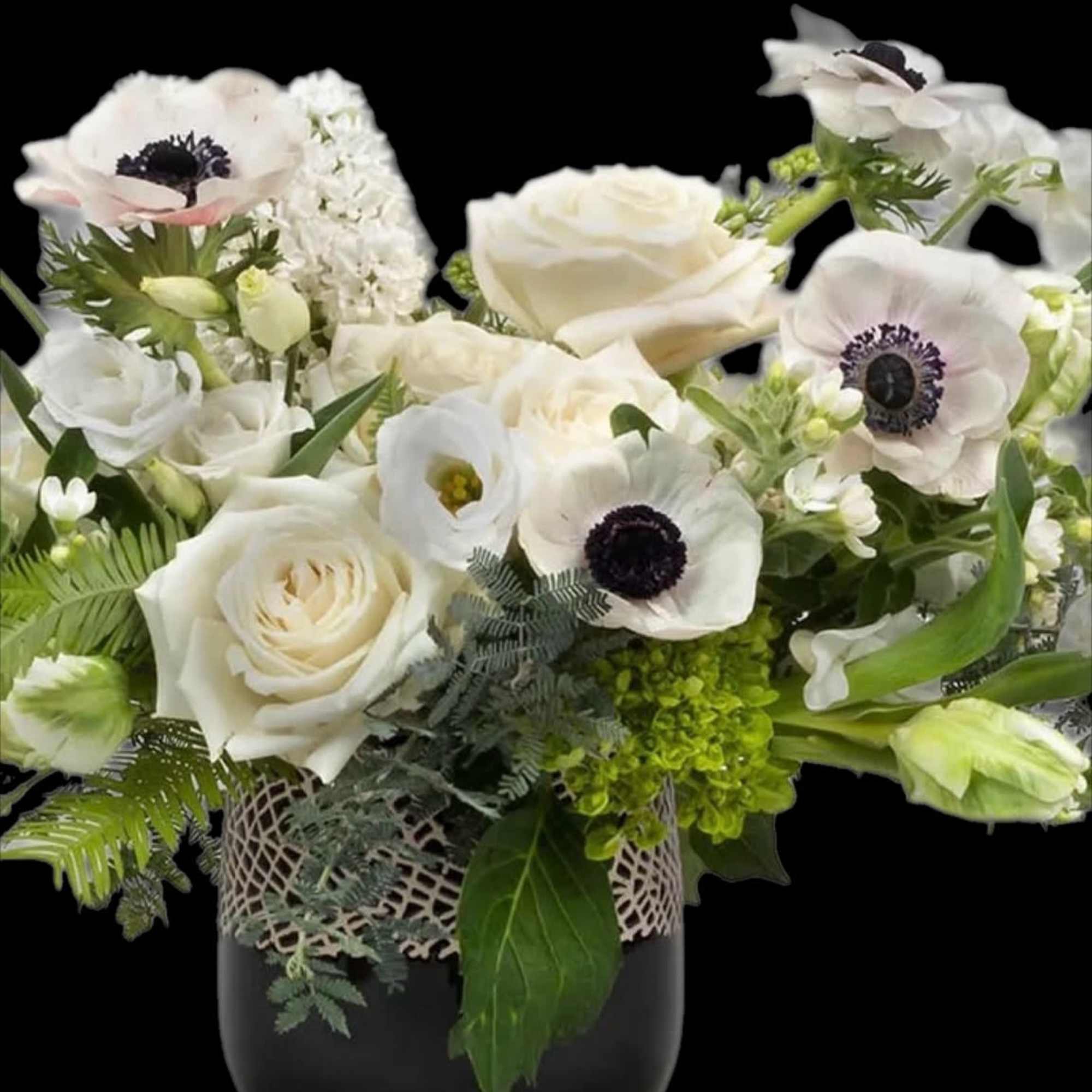 White floral arrangement in a black vase with green accents