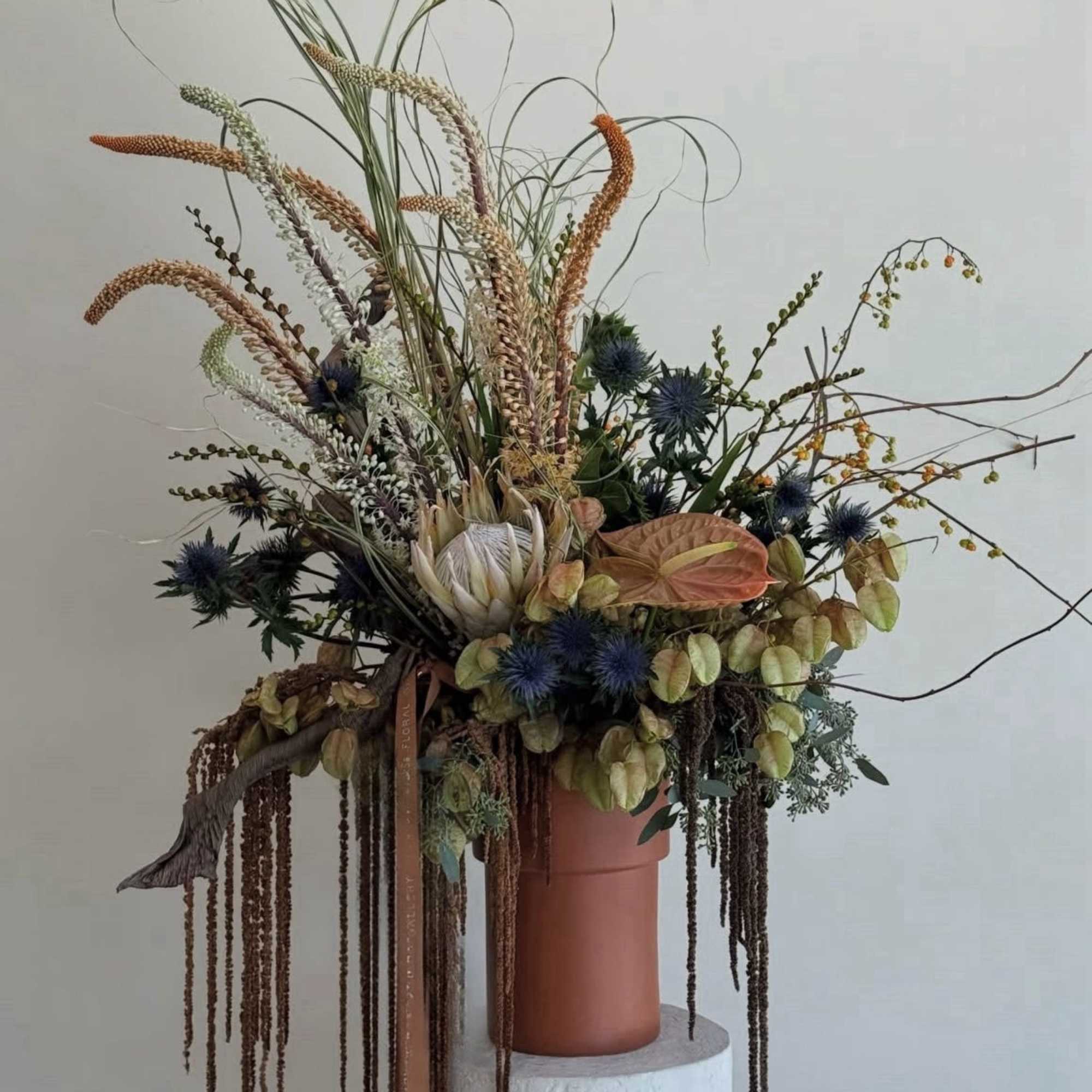 Tall dried floral arrangement in a terracotta vase with trailing elements