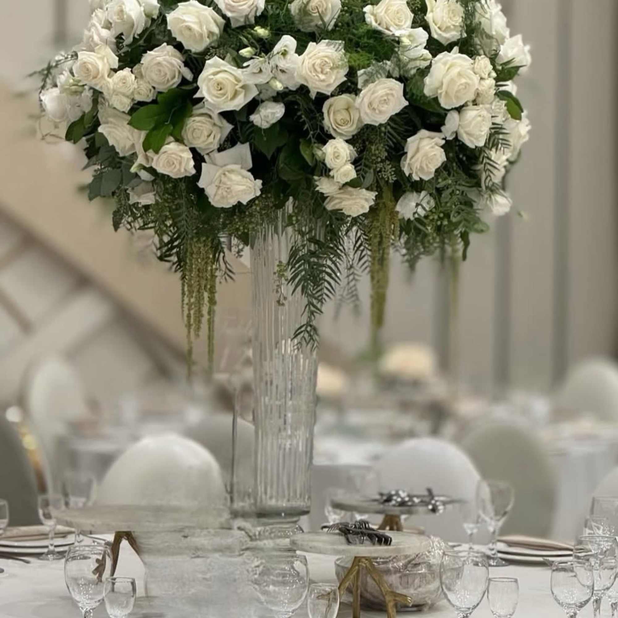 Tall white rose centerpiece in a clear glass vase on a banquet table
