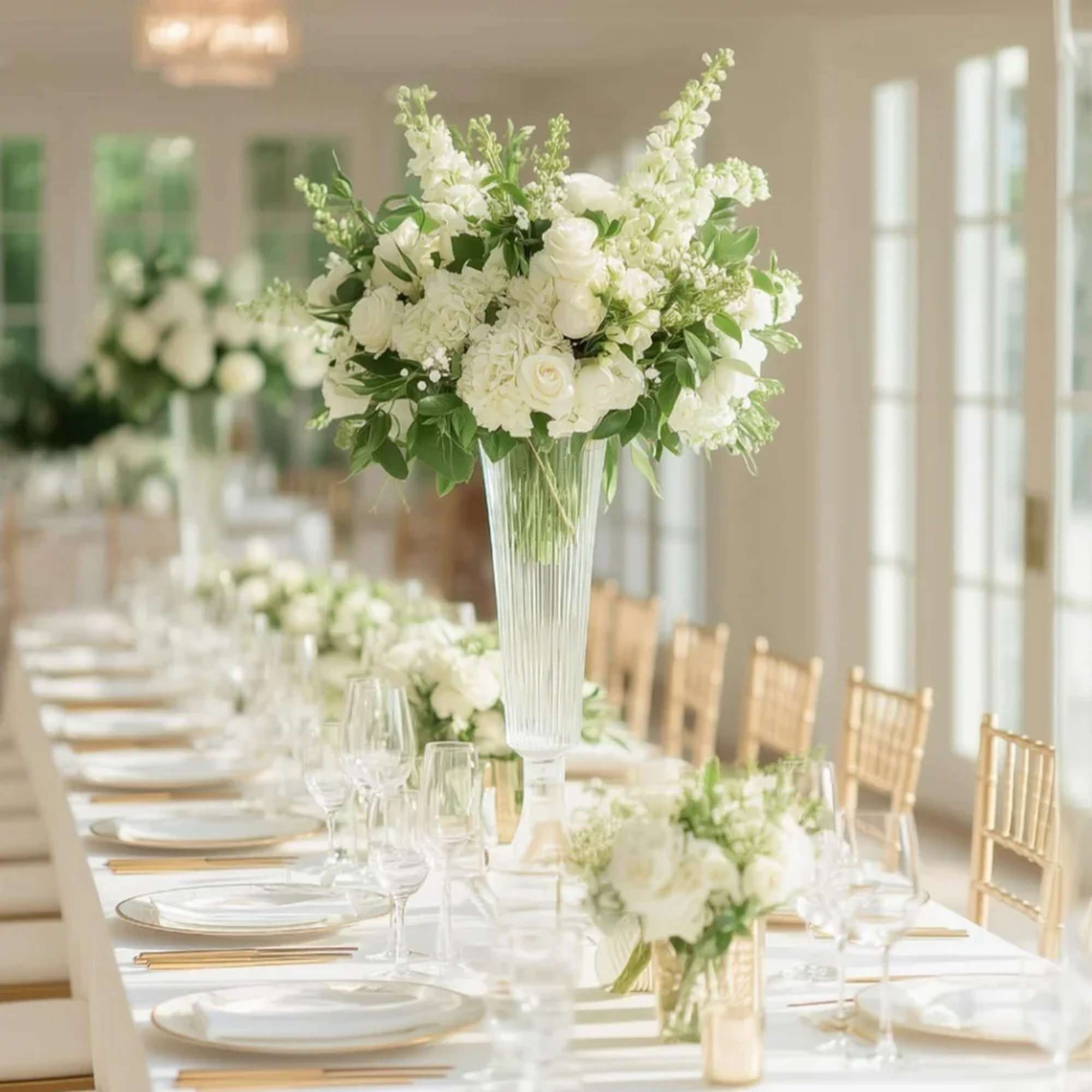White floral centerpiece in a tall clear vase on a set table