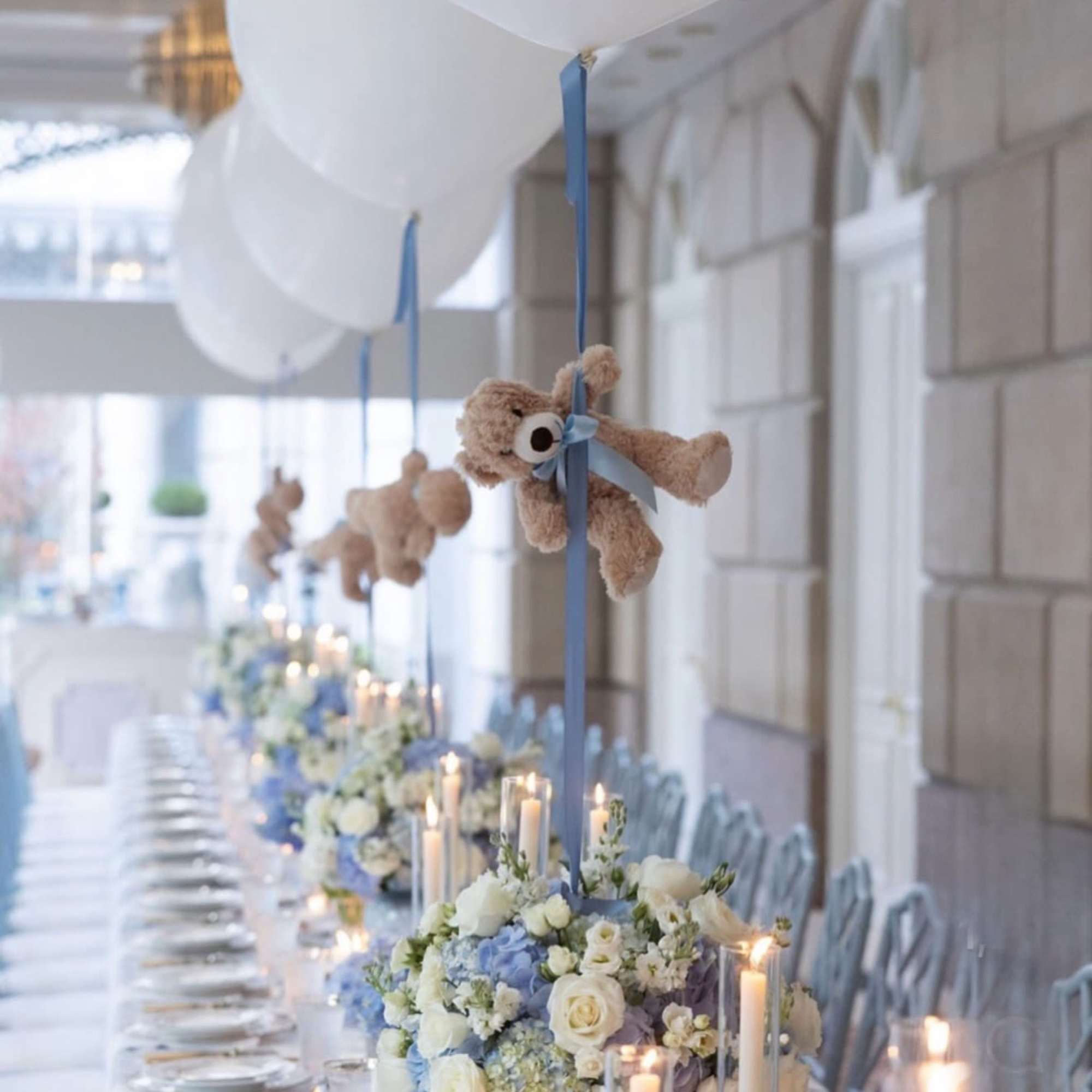 Blue and white floral centerpieces with teddy bears and balloons on a long table