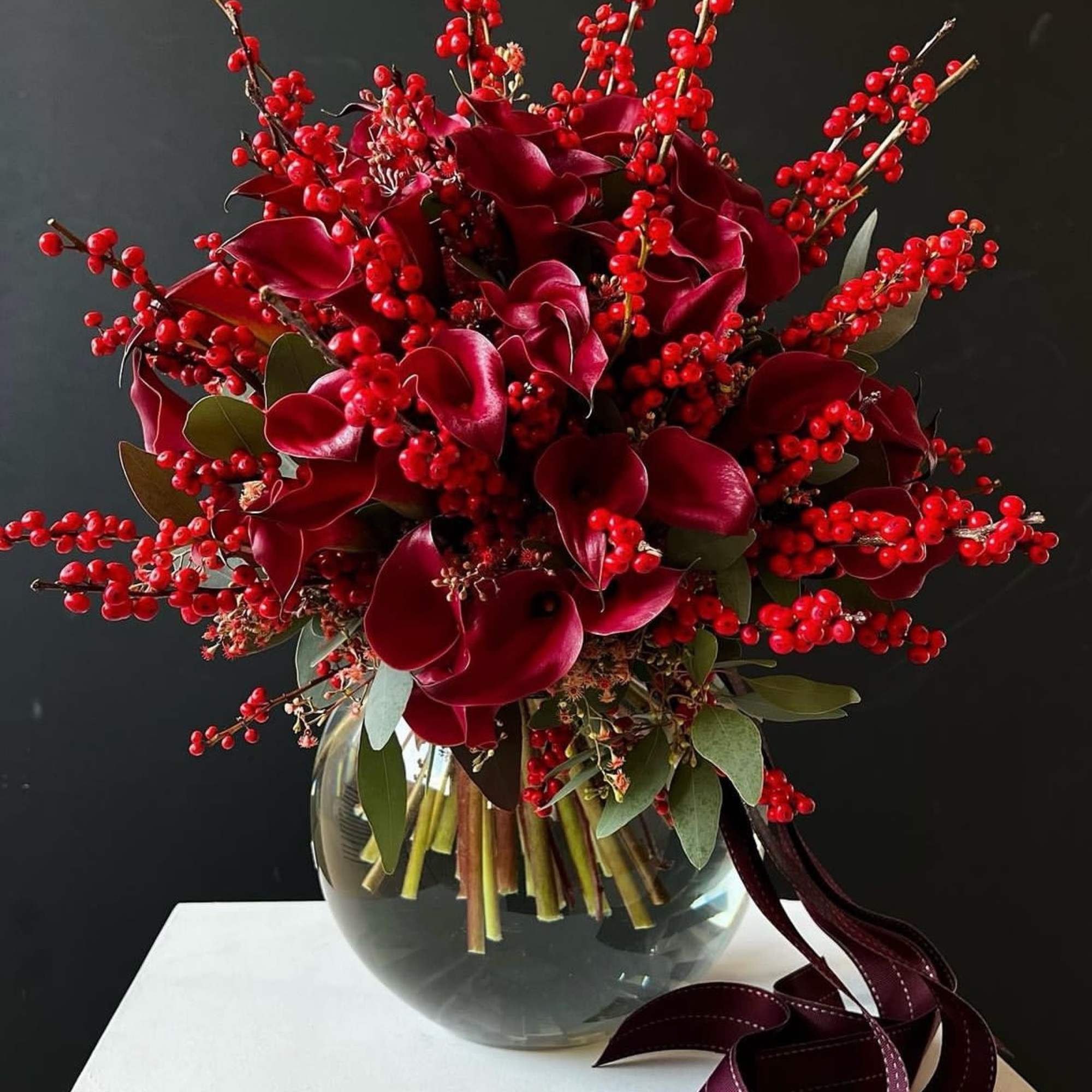 Red calla lily bouquet in a glass vase with berry branches