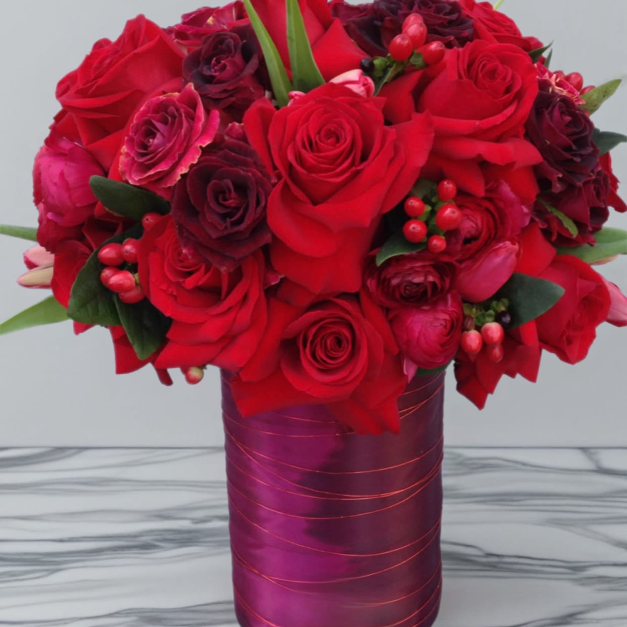 Red roses and dark burgundy blooms in a purple vase