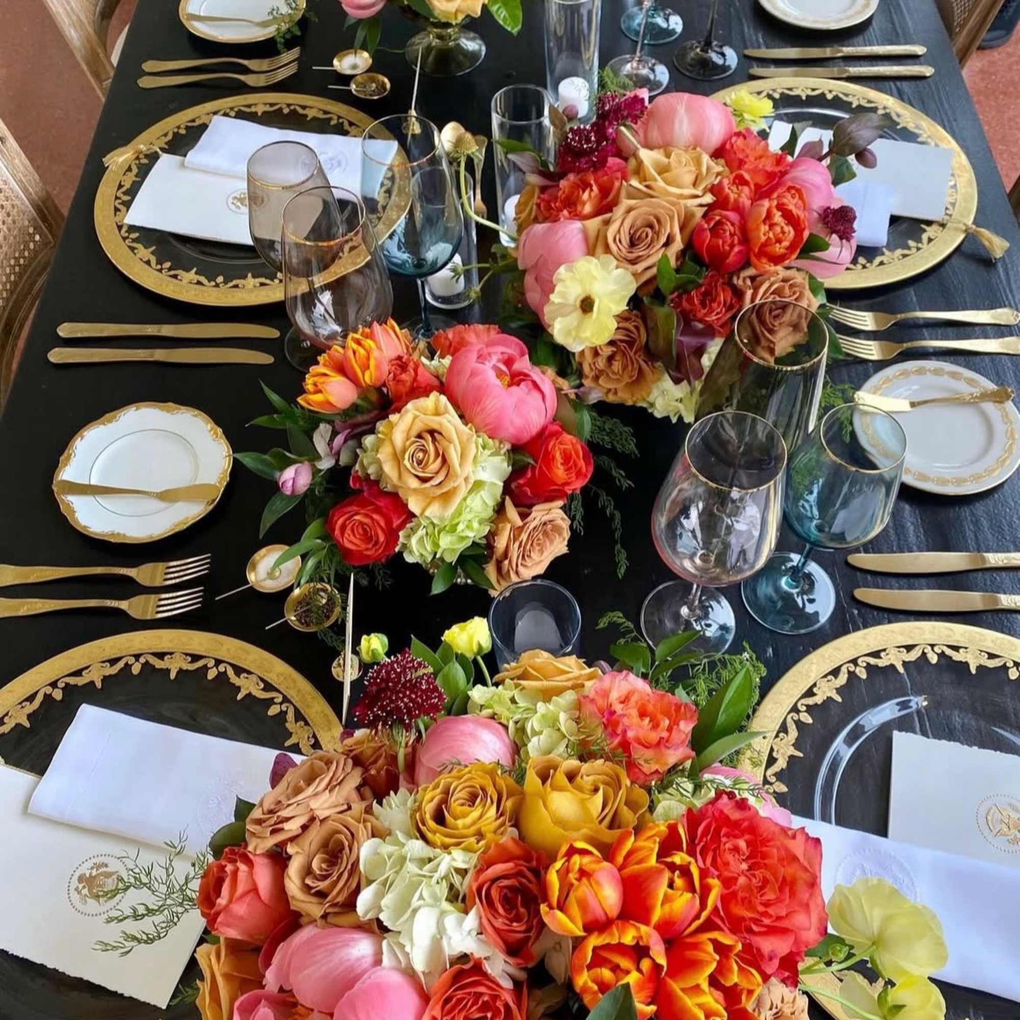 Floral centerpieces on a black-and-gold table setting with glassware and plates
