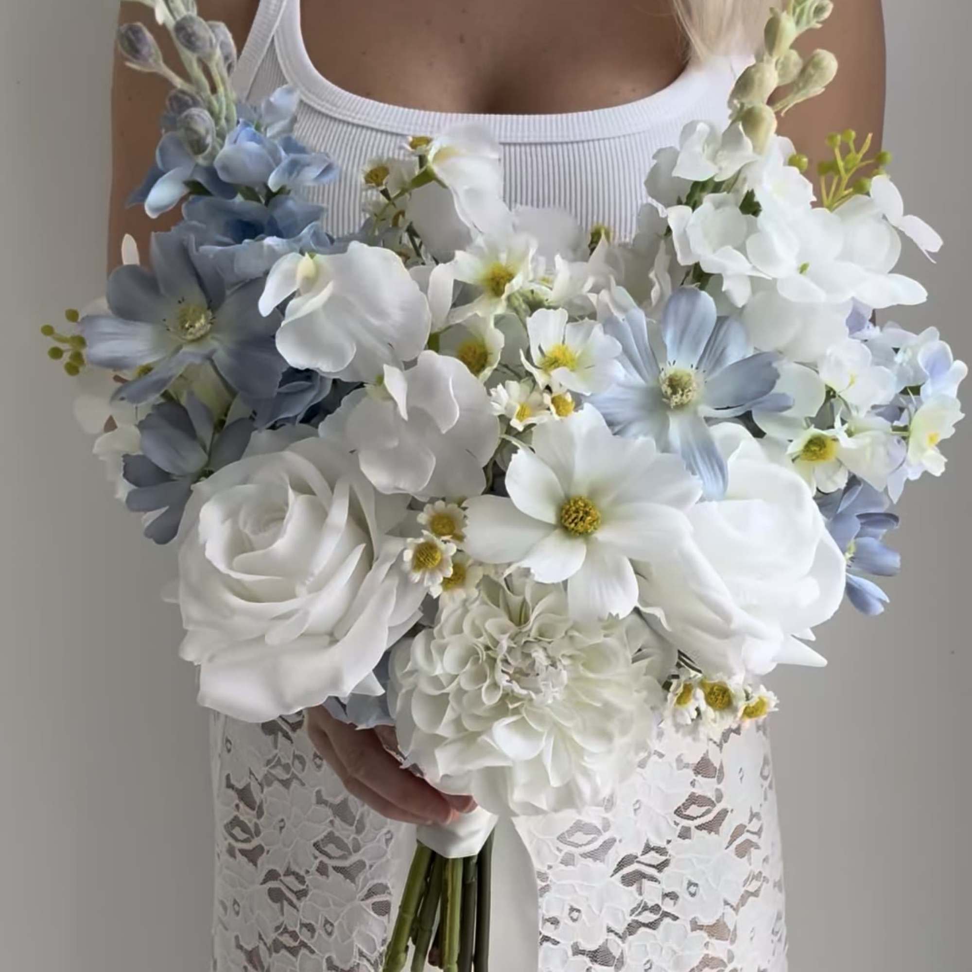 Bride holding a white and pale blue bouquet with roses and daisies
