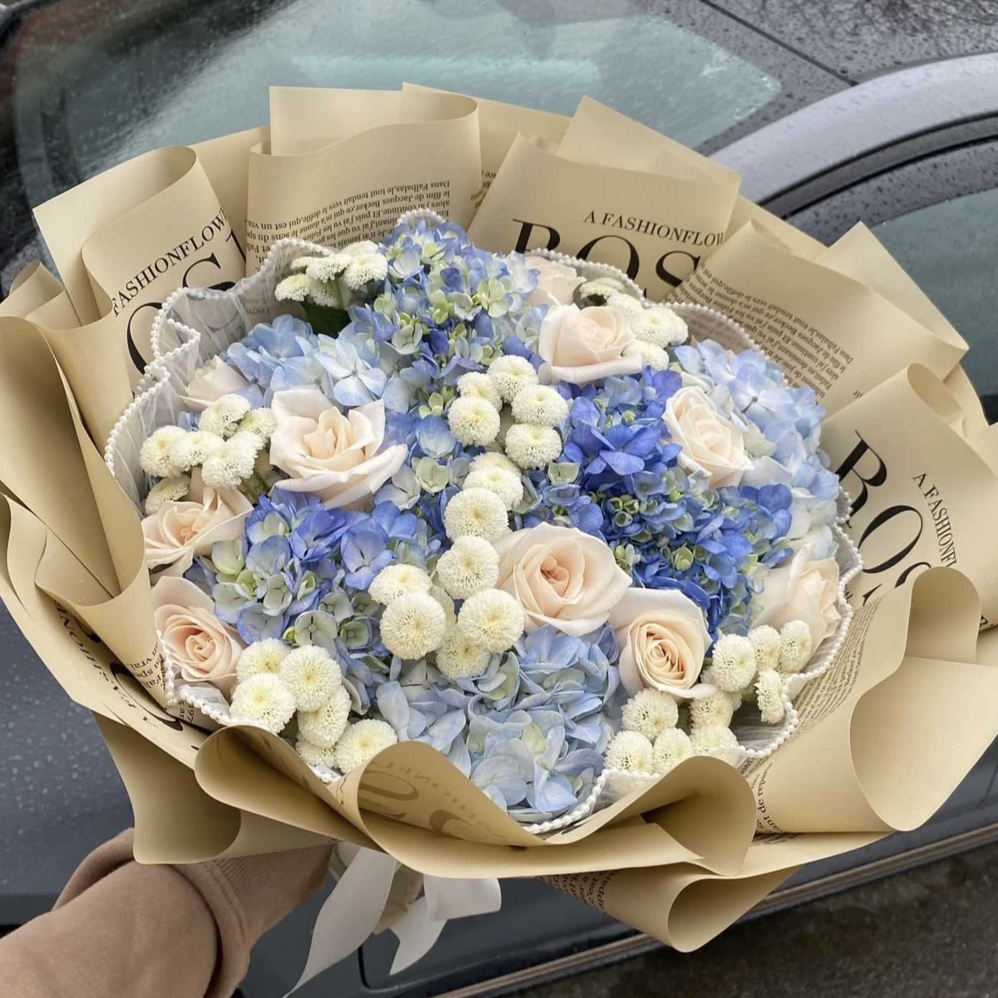 Bouquet of pale blue hydrangeas and blush roses wrapped in tan paper