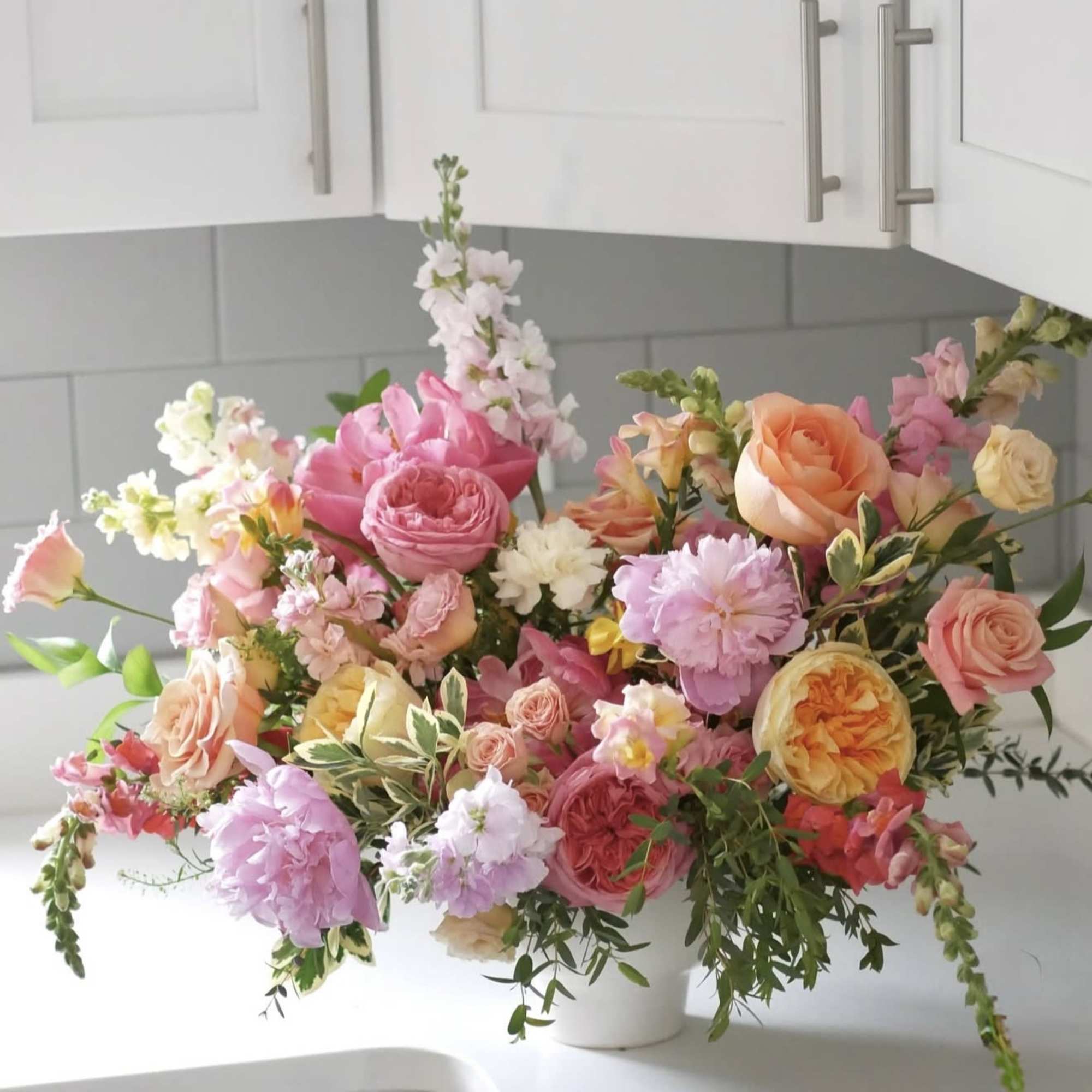 Mixed bouquet of pink, peach, and white flowers in a white vase