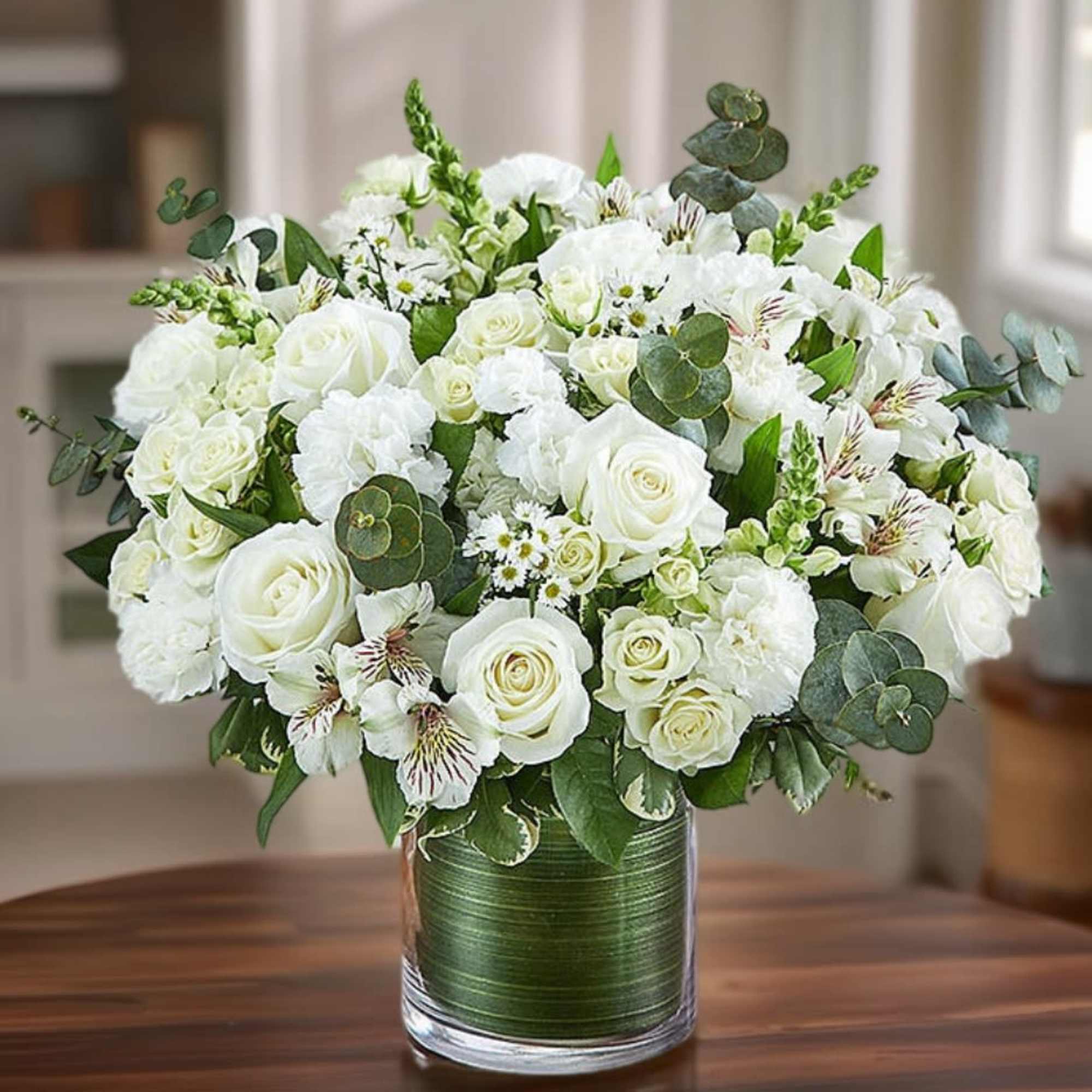 White rose bouquet in a glass vase with green foliage