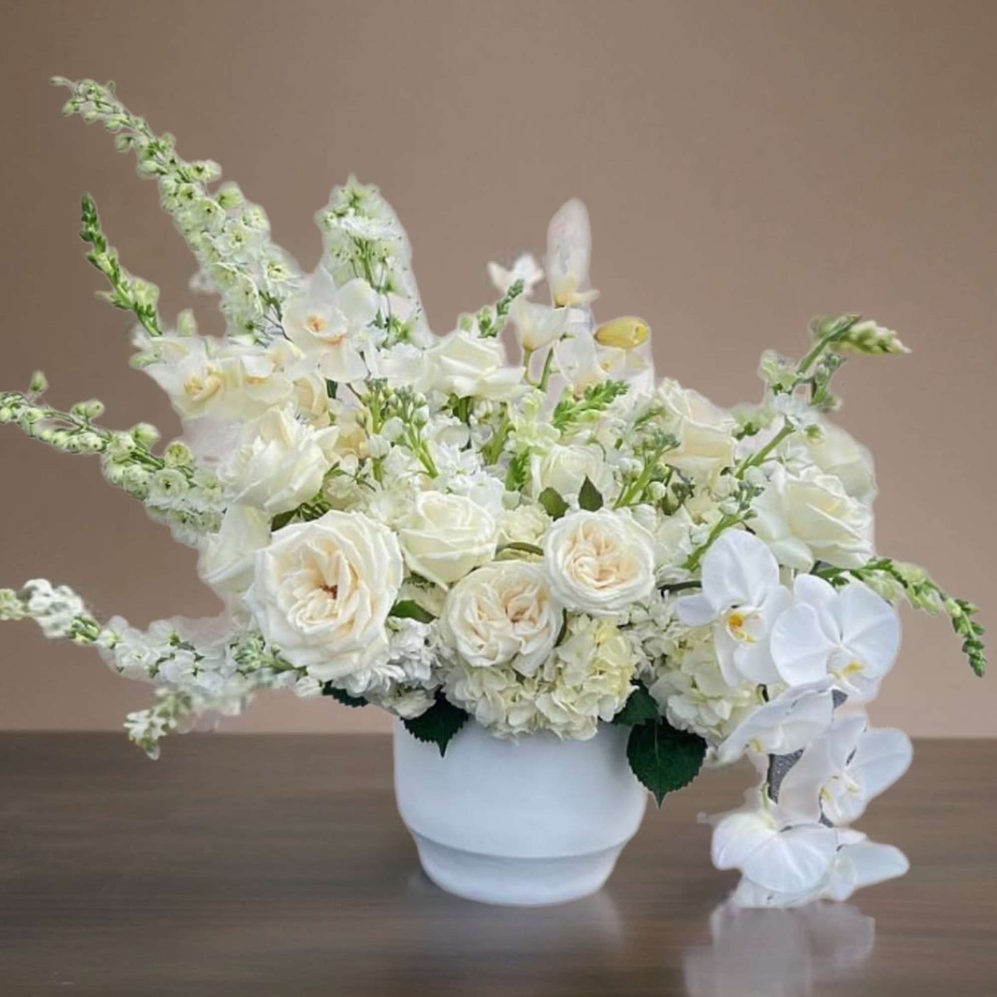 White floral arrangement in a white vase with roses and orchids