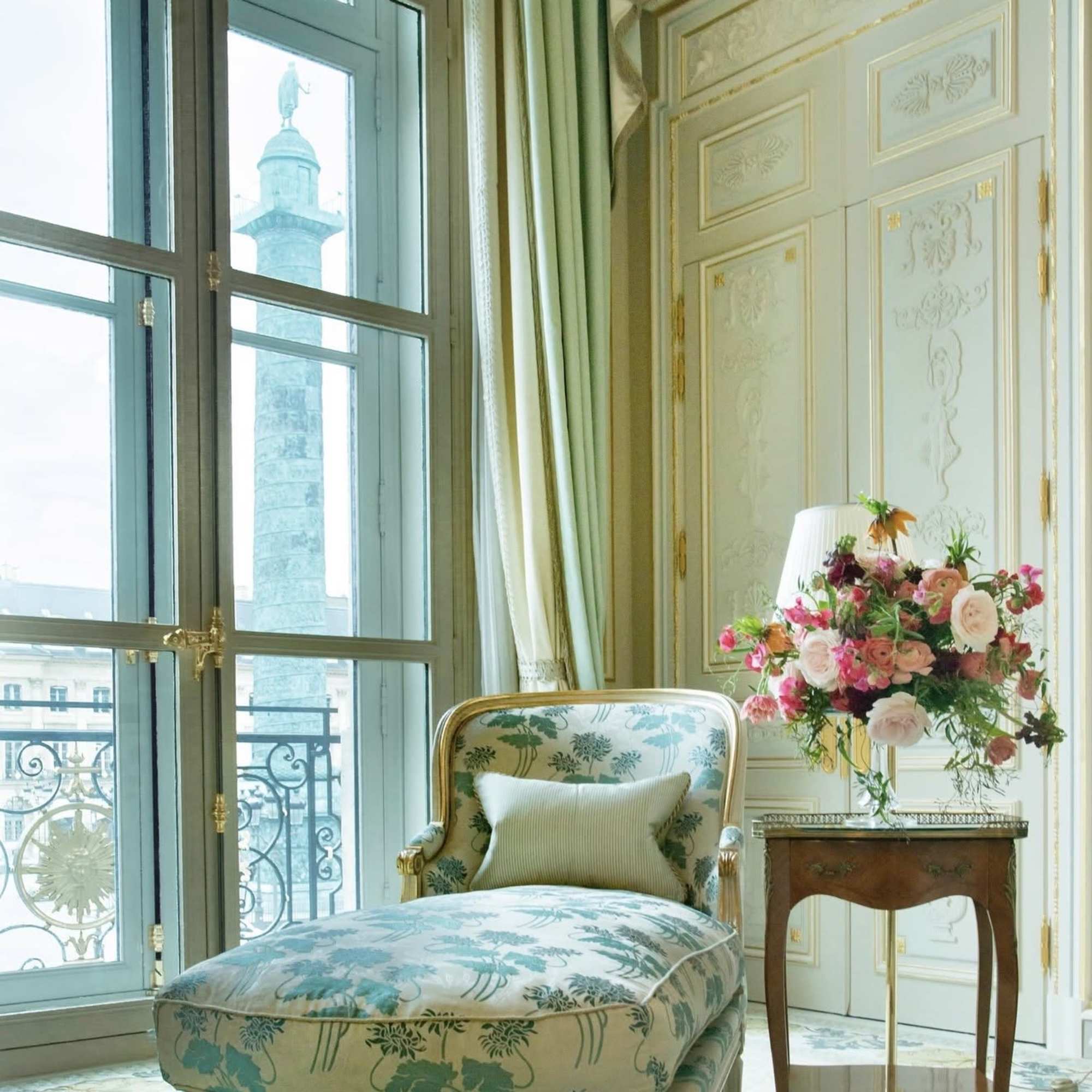 Pink and white floral arrangement on a side table beside an upholstered chair