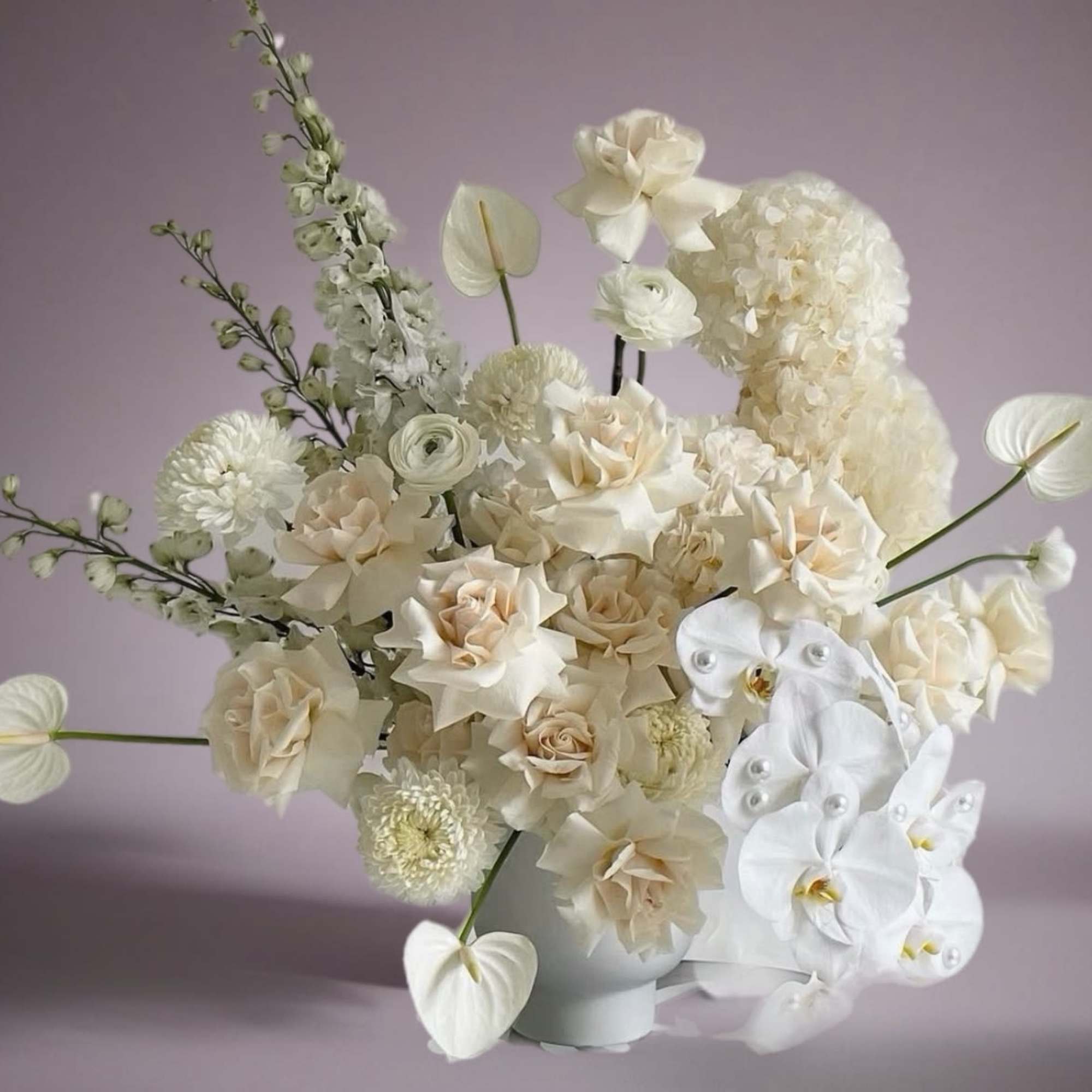 Cream and white floral arrangement in a white vase with orchids and roses