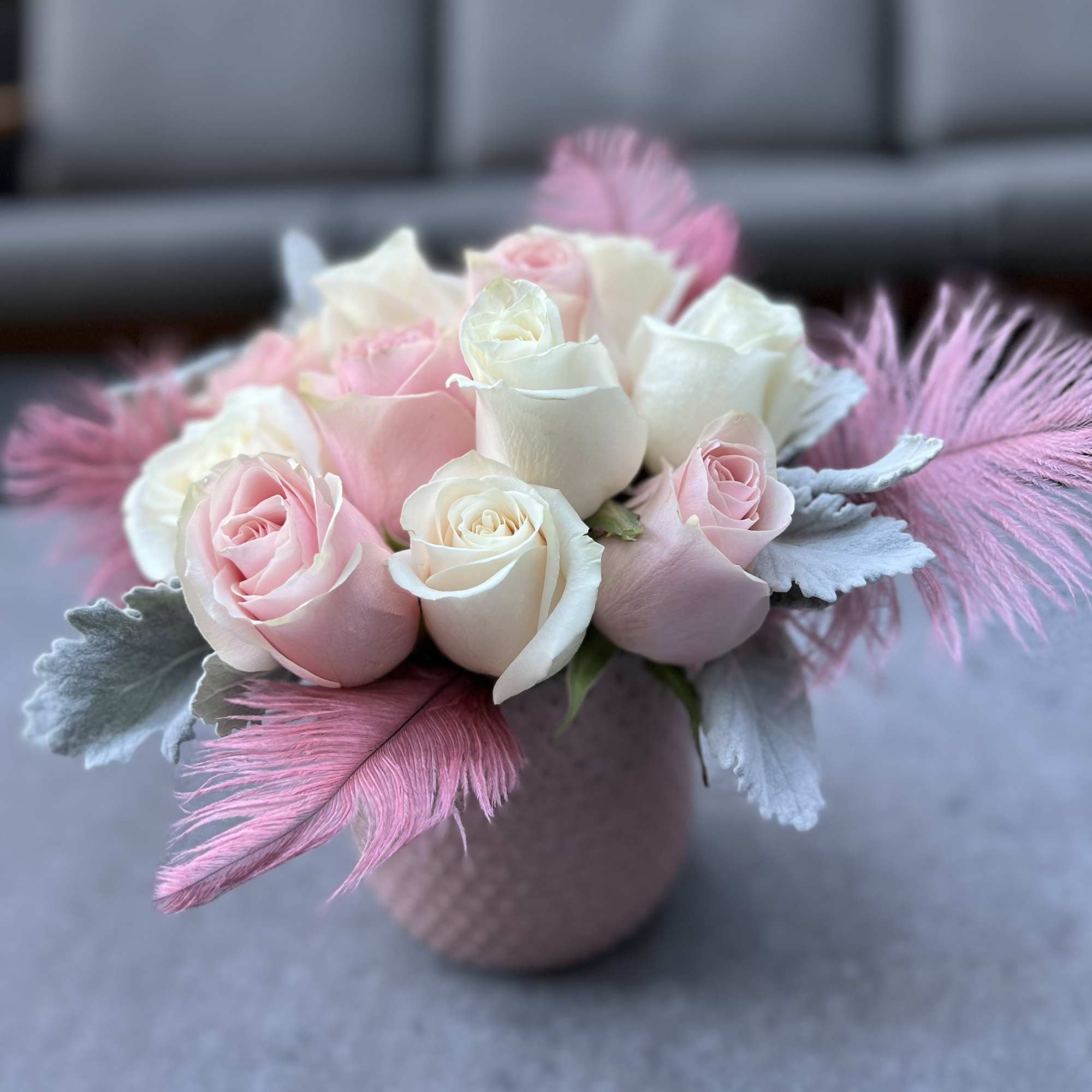Pink and white rose arrangement in a textured vase with feathers