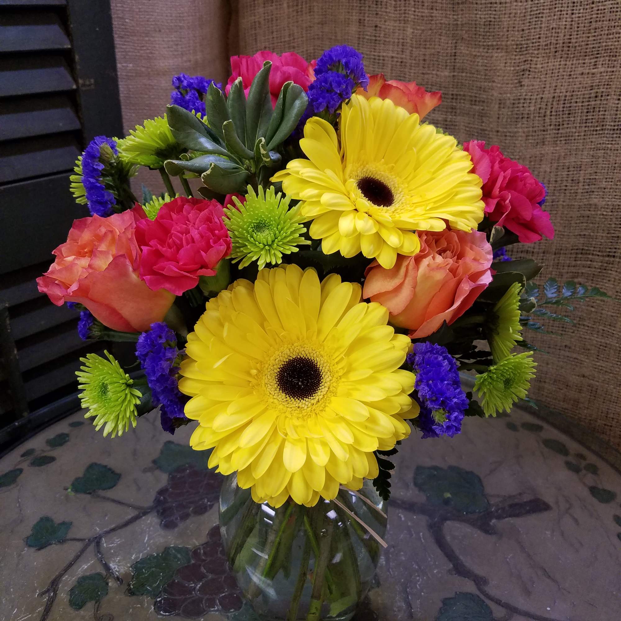 Bright mixed bouquet with yellow gerbera daisies, roses and carnations in a clear glass vase